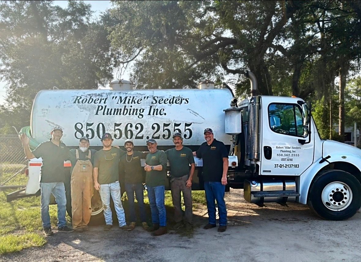 Plumbing company crew posing beside a white service truck in a wooded yard.