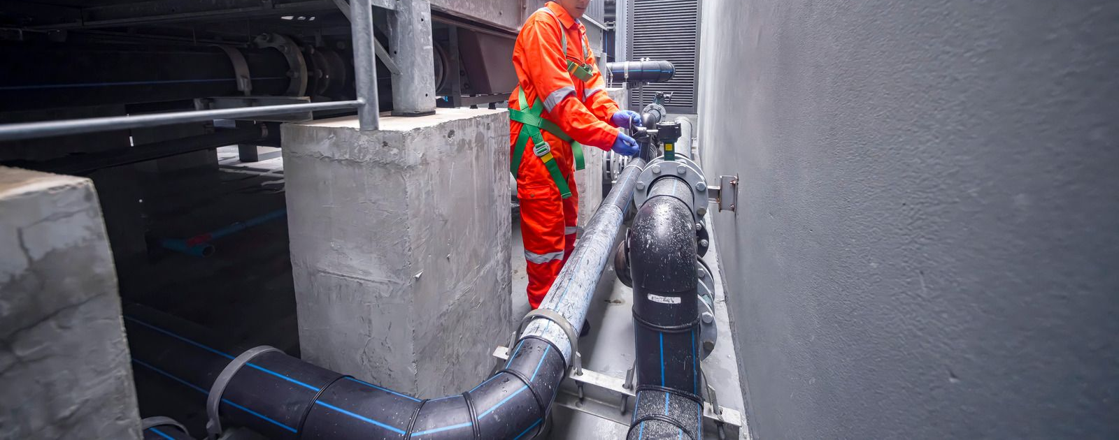 Worker in orange safety gear inspecting large pipes in an industrial facility