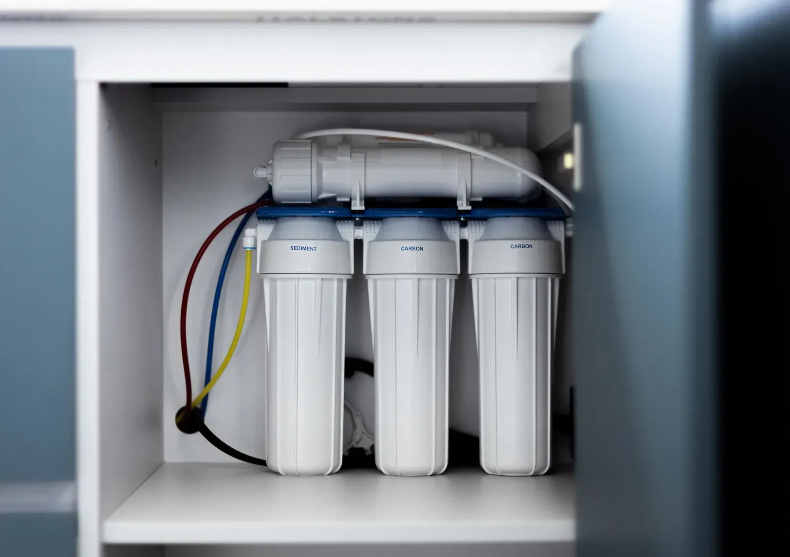 Three white water filters inside an open cabinet with colored tubing and fittings