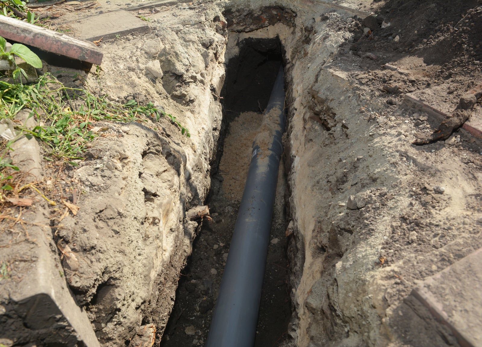 Hands installing underground wiring in a trench beside concrete slabs and PVC pipe connectors