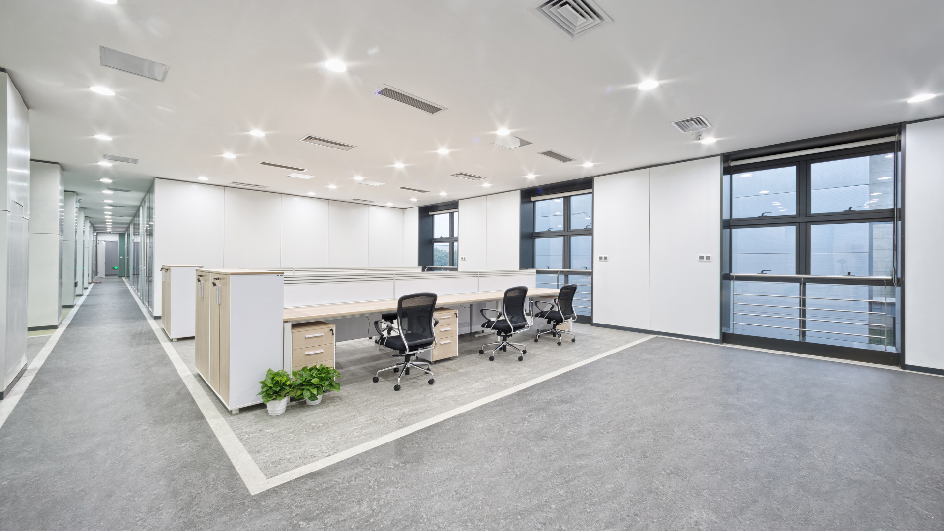 Modern open-plan office with desks, chairs, and bright windows overlooking a city view