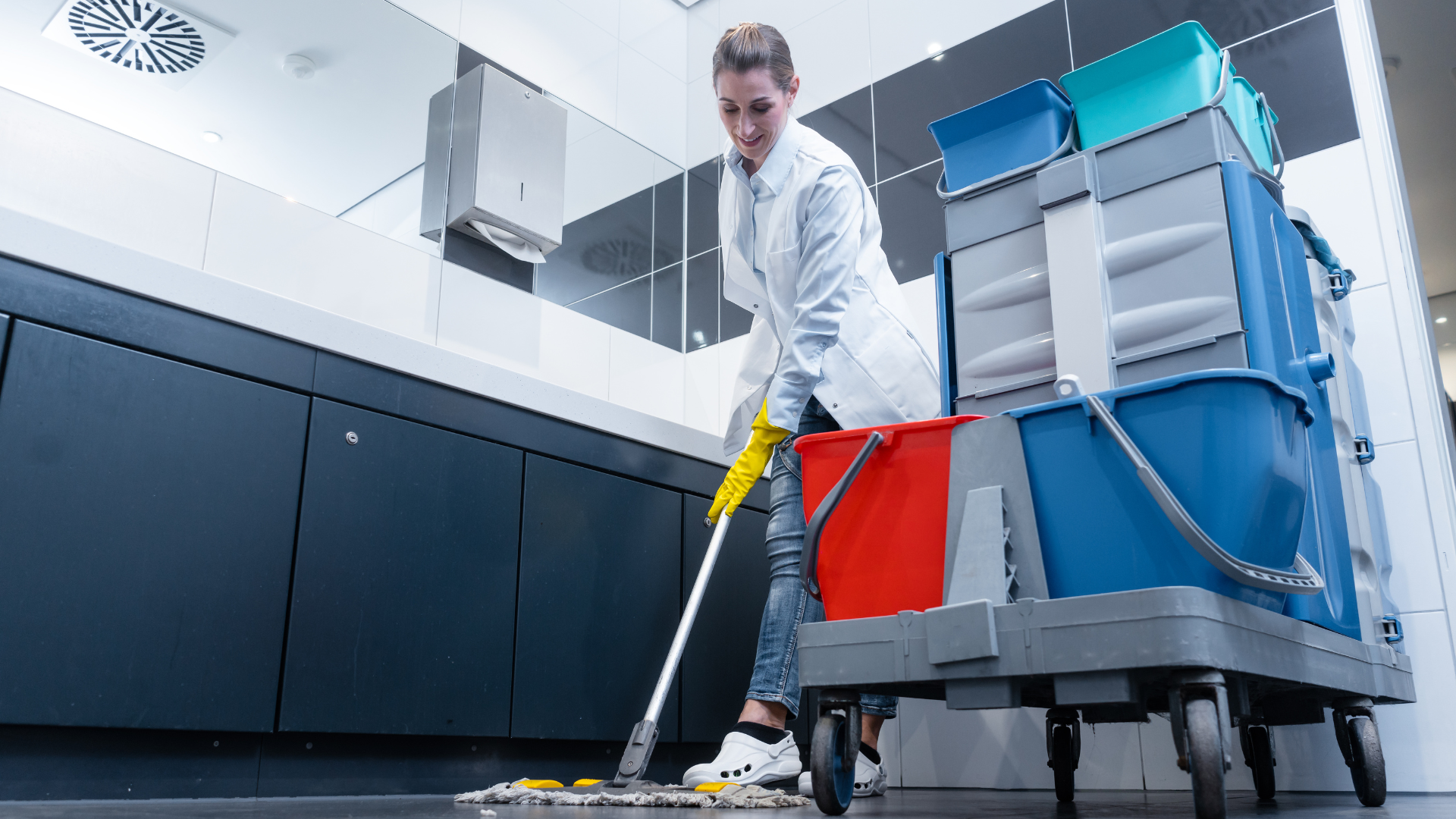 Janitor mopping a clean industrial floor beside a cart of cleaning supplies