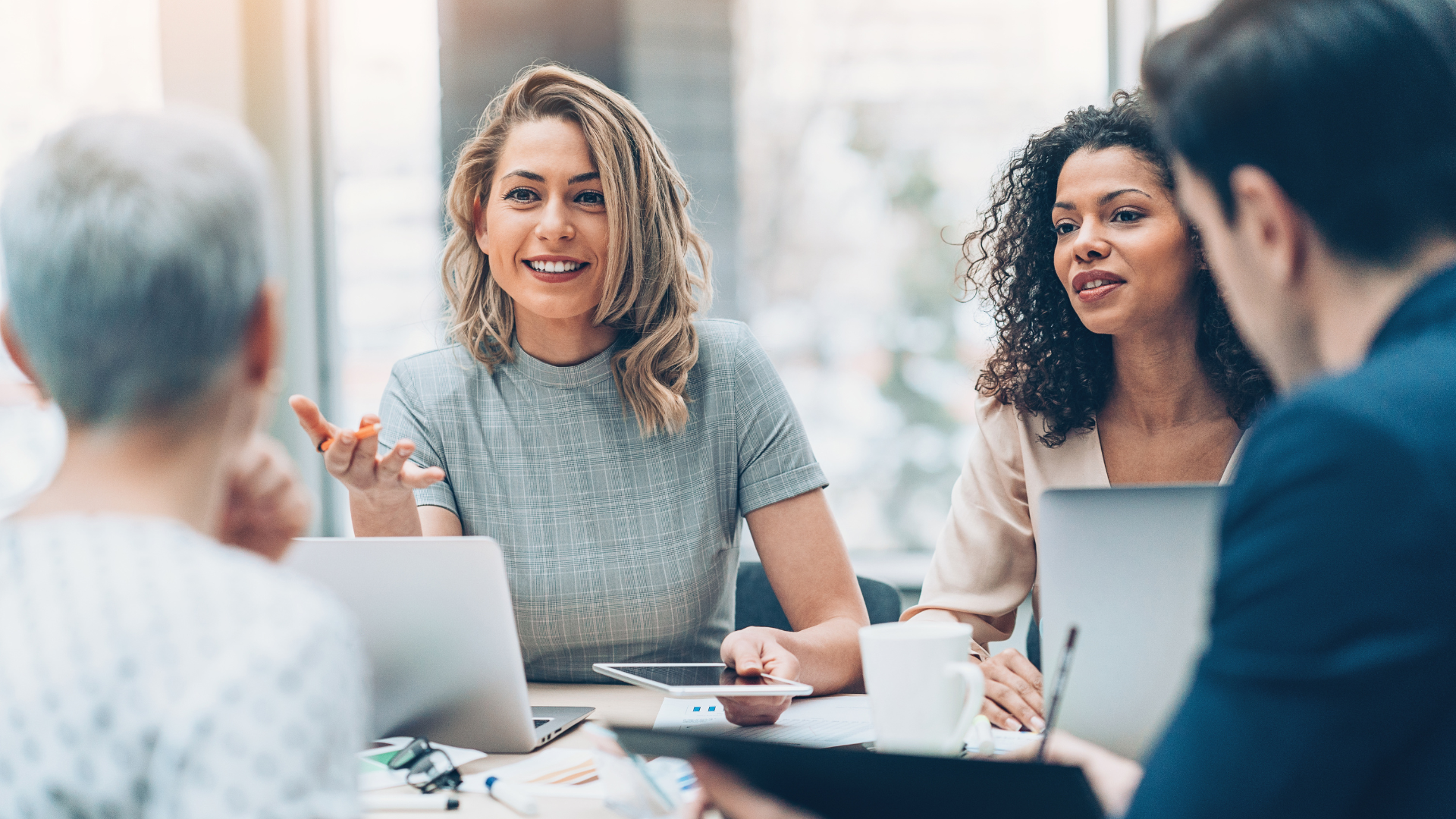 Small business team meeting around a table, with laptops and smiling discussion in a bright office.