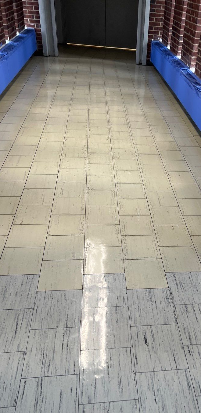 Empty tiled hallway with blue side barriers and brick walls, lit by overhead lights