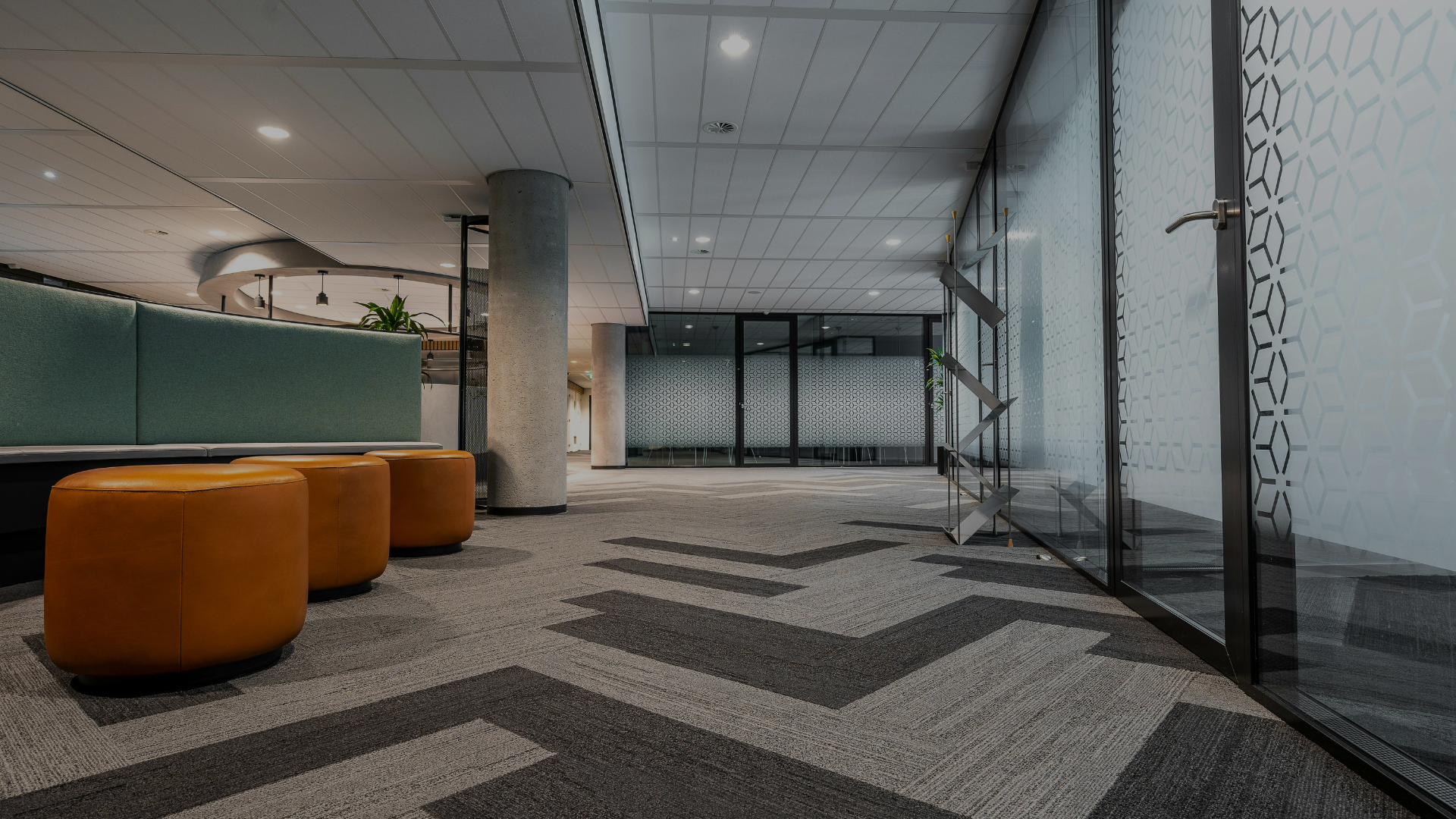 Modern office lobby with orange stools, glass walls, and patterned carpet leading to a doorway