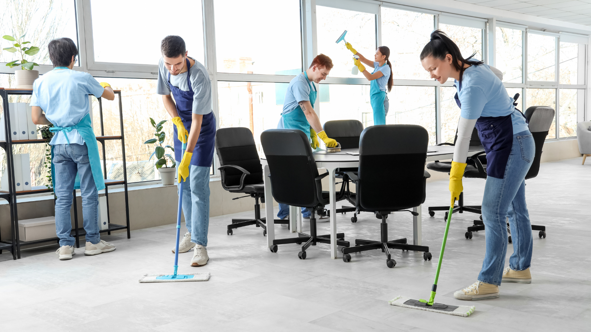 Office cleaning crew mopping a bright conference room with desks and black chairs.