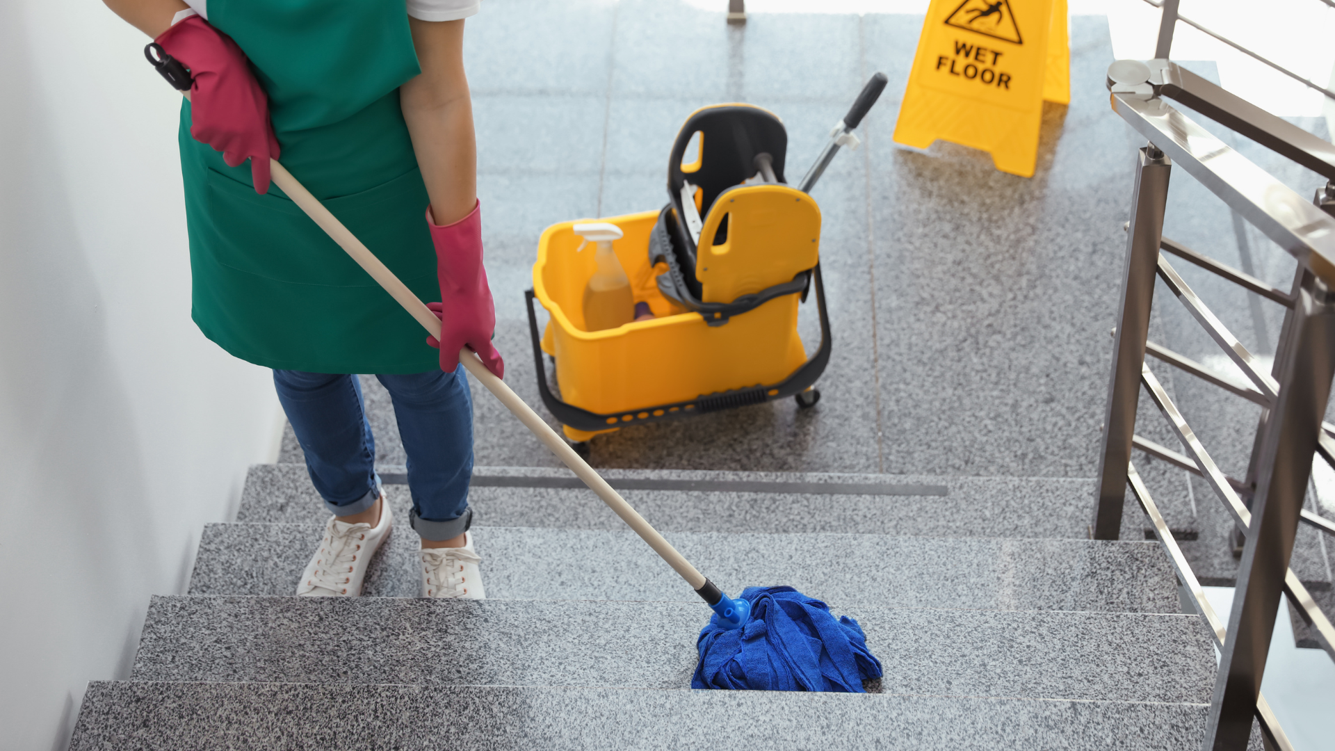 Person mopping a stairway beside a yellow cleaning cart and wet floor sign