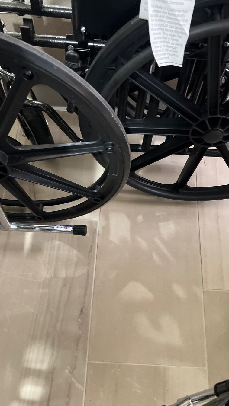 Two black wheelchair wheels on a glossy tiled floor, with a metal footrest visible.
