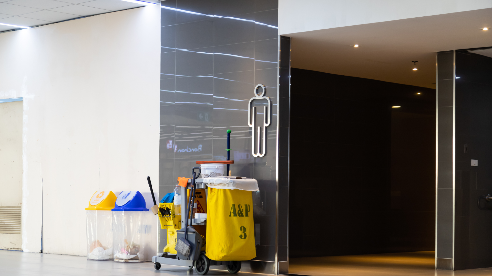 Restroom entrance with a men's symbol, cleaning cart, and waste bins.