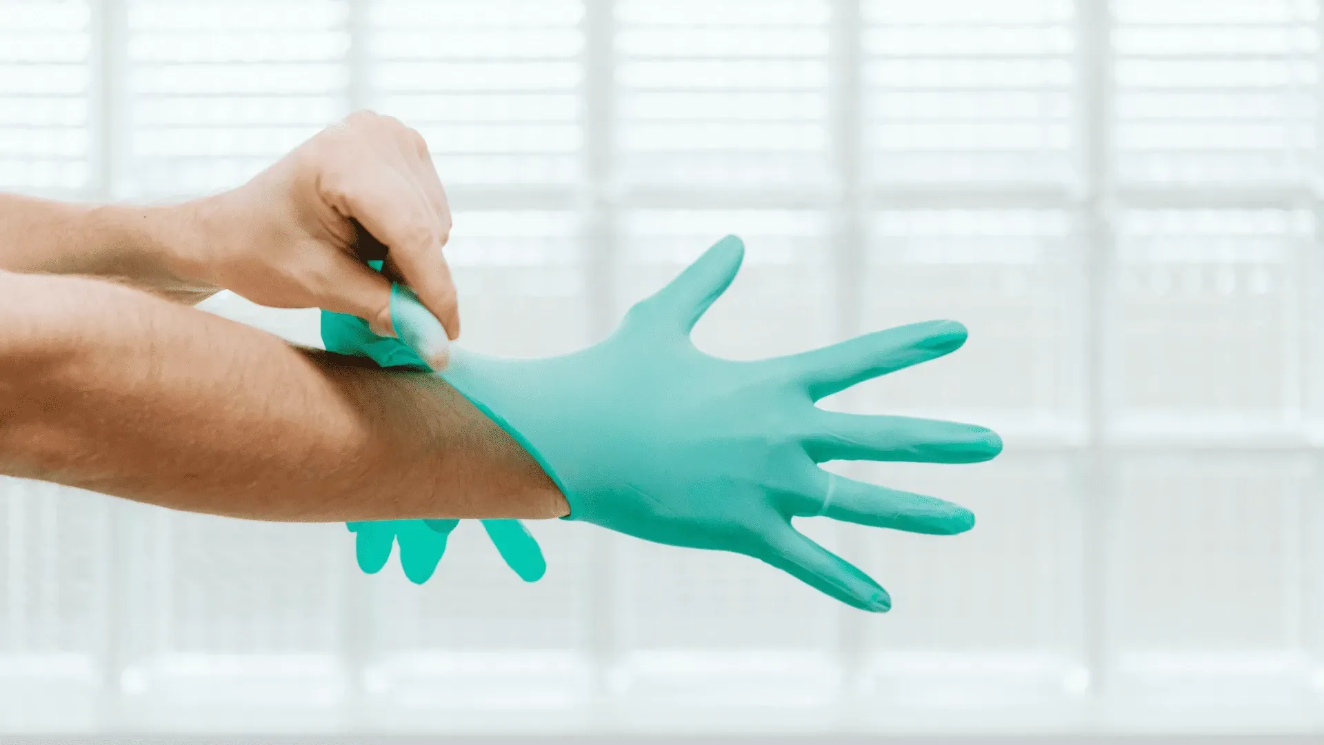 Person putting on a blue latex glove. Against a white, textured background.