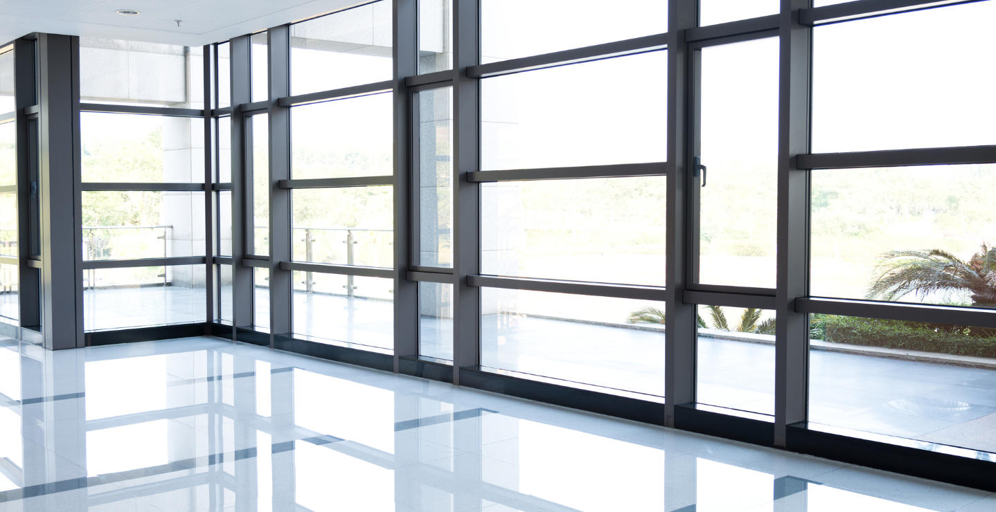 Bright, modern interior with large, grid-like windows and a glossy white floor; outside, glimpses of greenery.