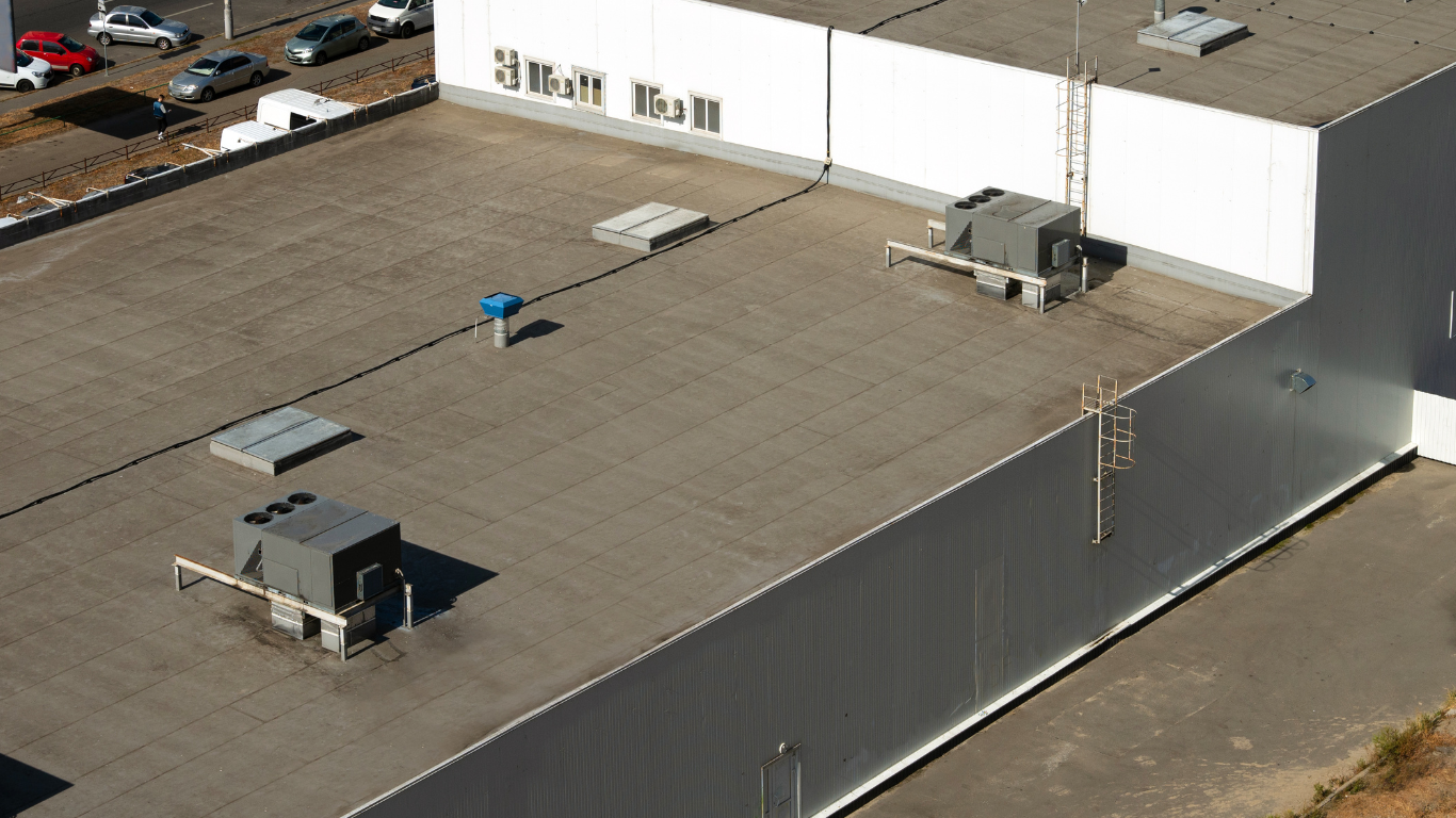 Aerial view of a flat industrial rooftop with HVAC units and vents on a white warehouse building.