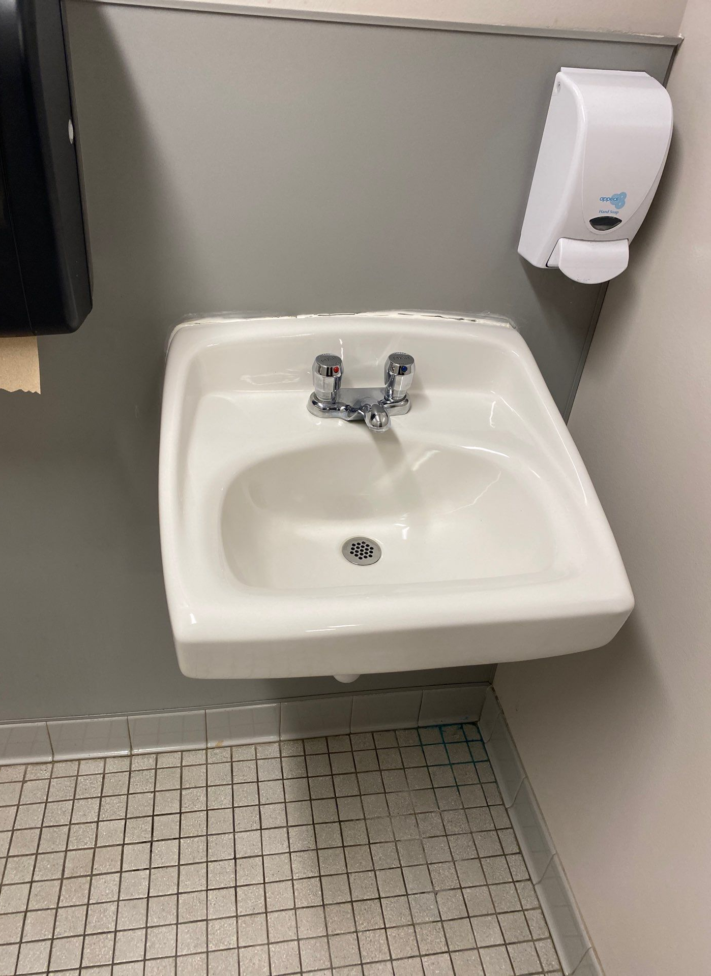 Small white bathroom sink with chrome faucet beside a wall-mounted soap dispenser.