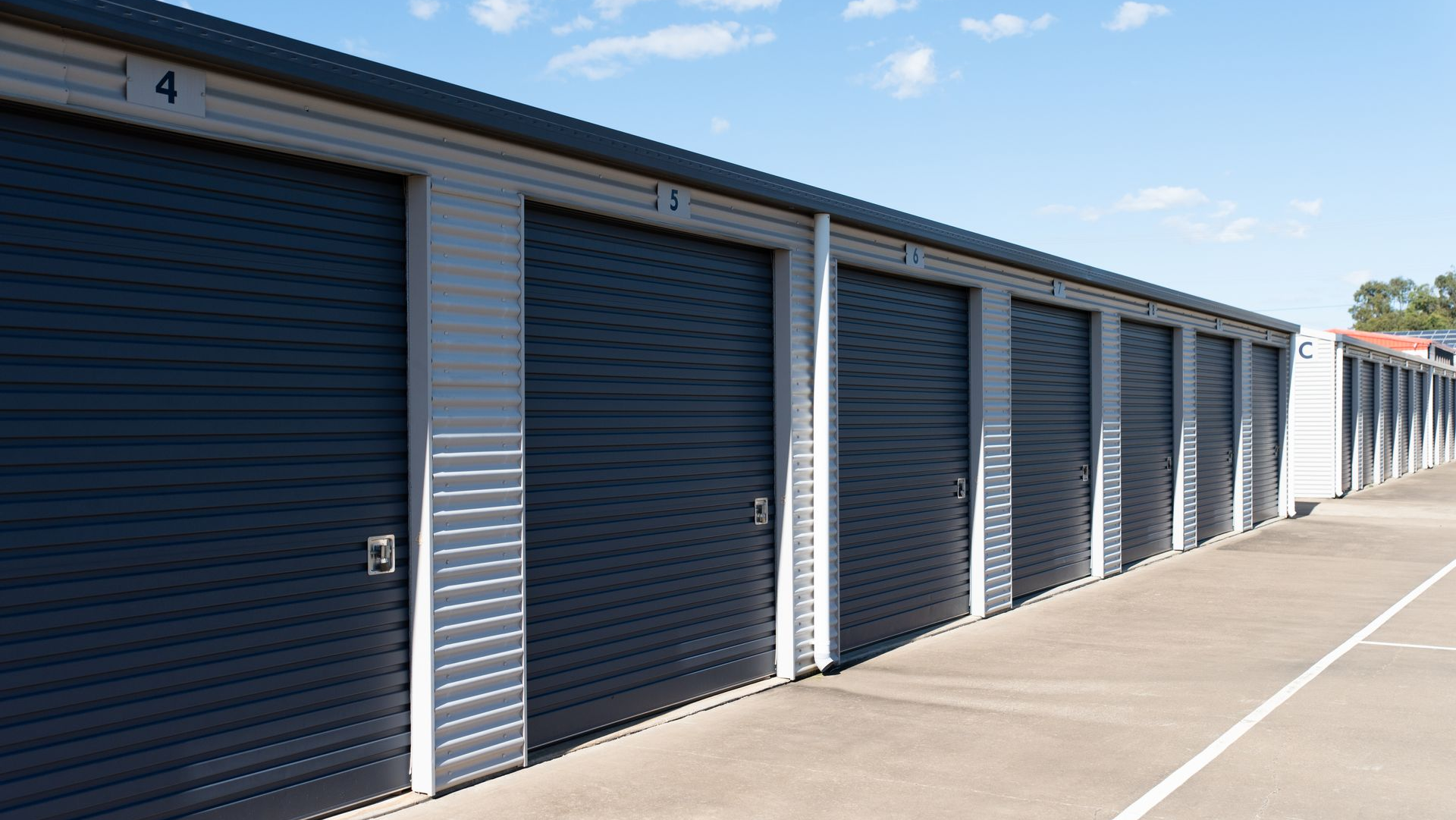 Row of gray storage unit doors along a sunny concrete driveway