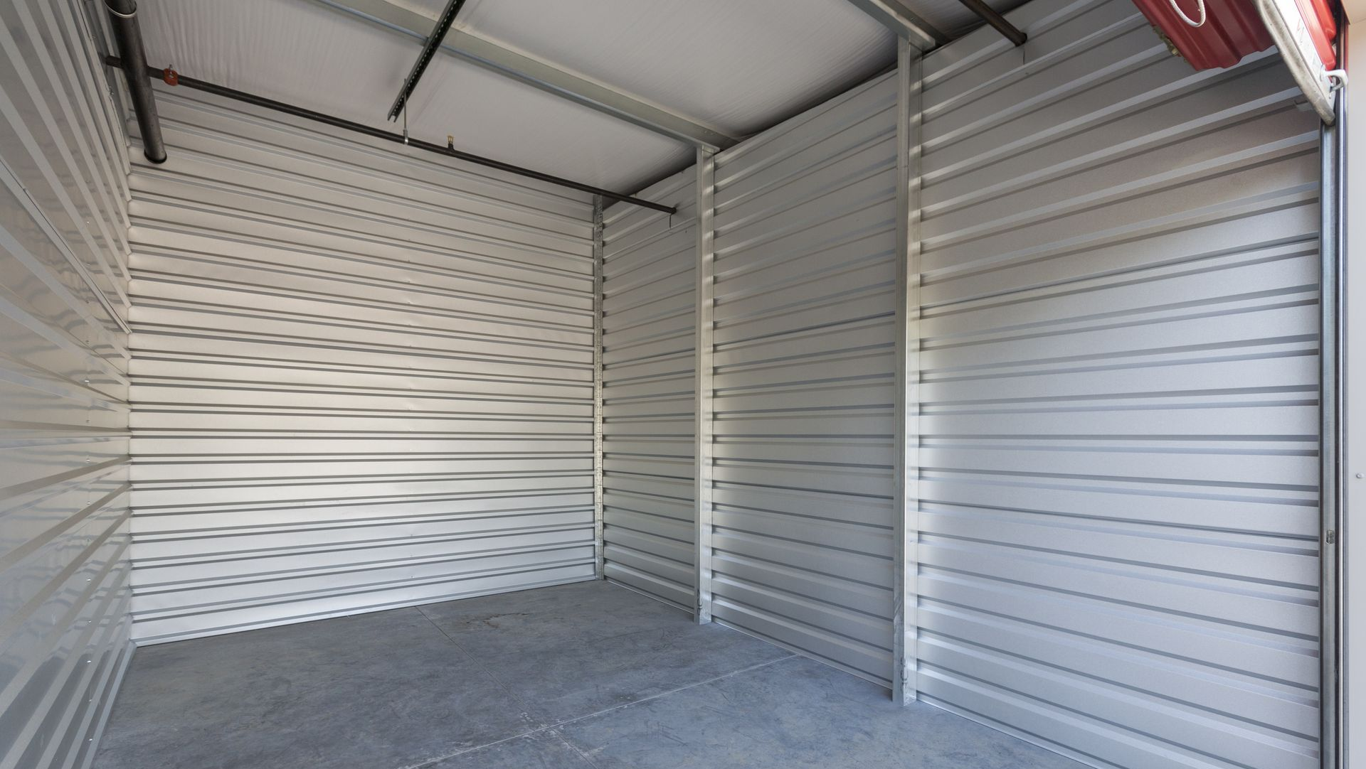 Empty metal storage unit with white corrugated walls and concrete floor