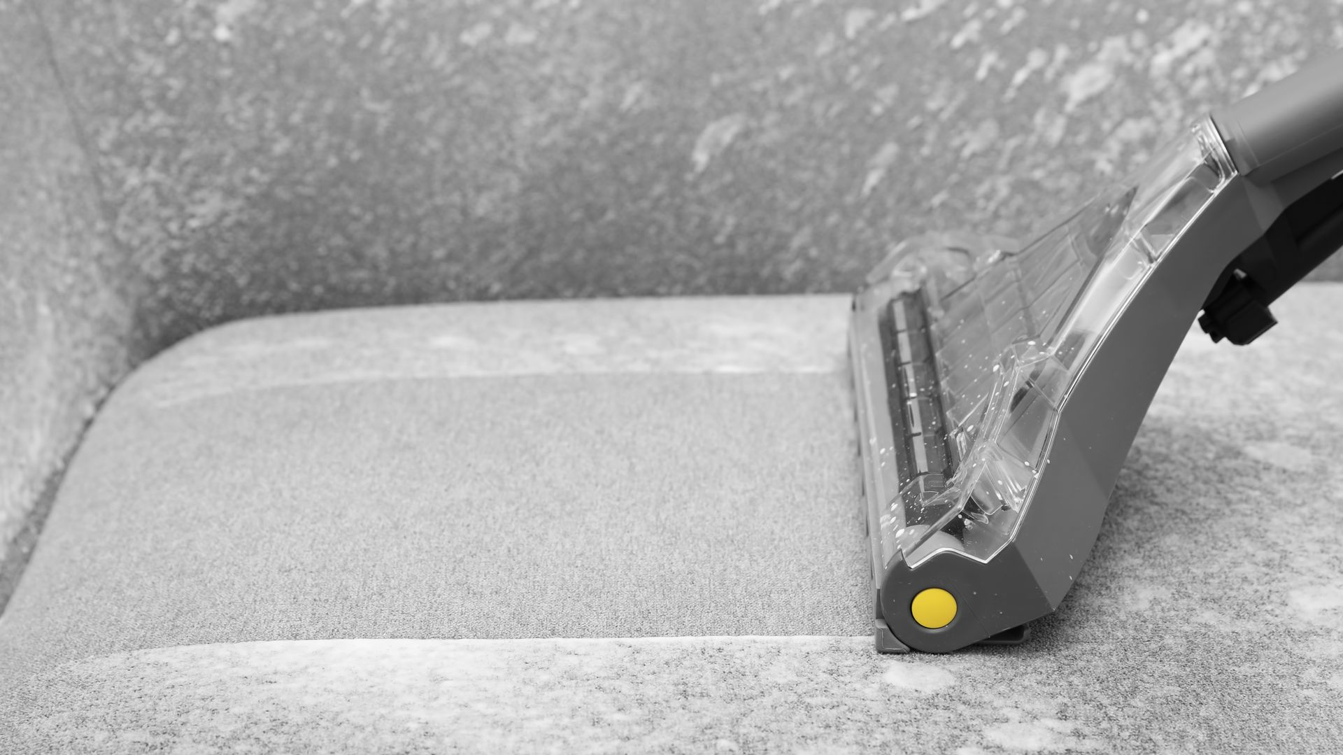 Close-up of a gray vacuum head cleaning a light gray carpet edge near a wall.
