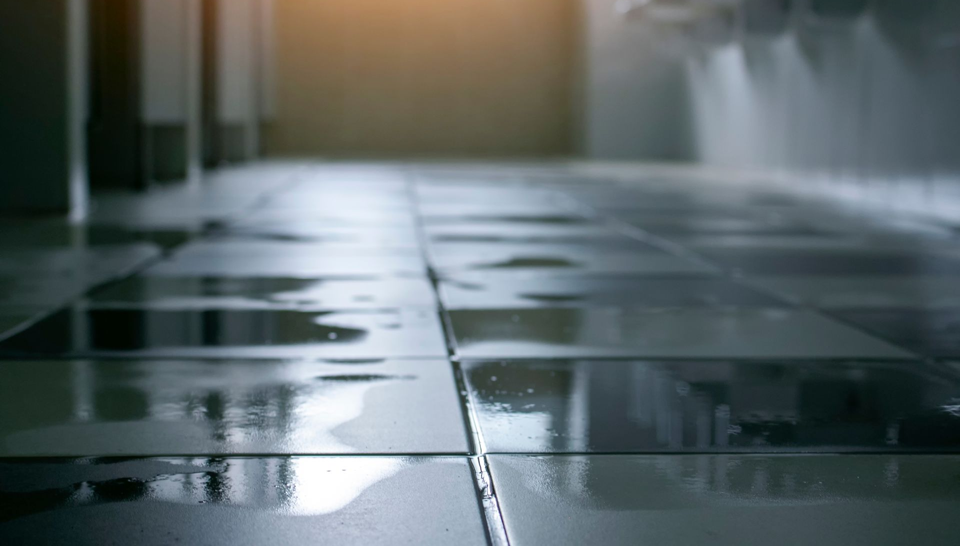 Empty wet tiled floor in a dim room with light streaming in from a doorway