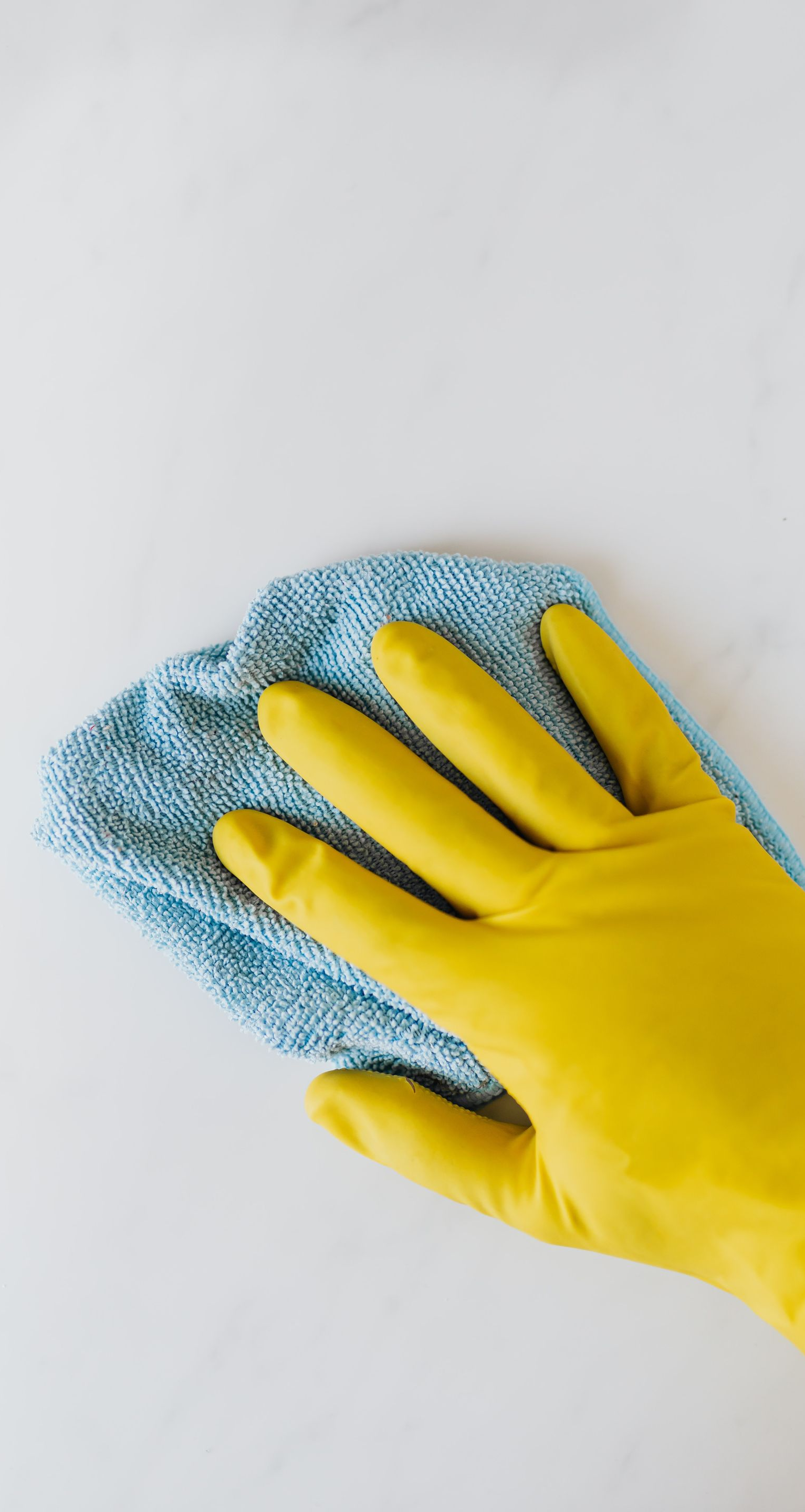 Yellow-gloved hand wiping a surface with a blue microfiber cloth