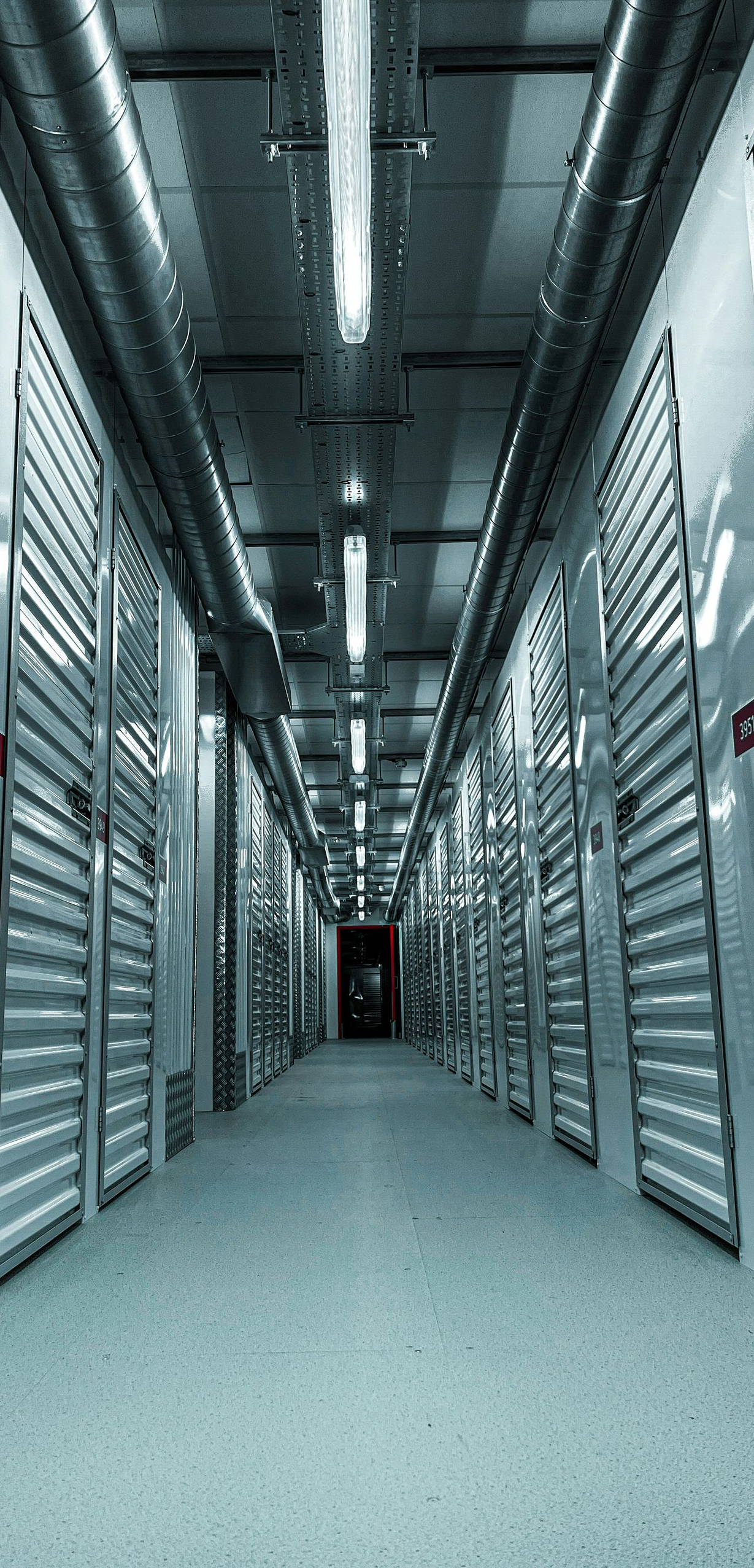 Long, empty storage corridor with metal lockers and overhead fluorescent lights