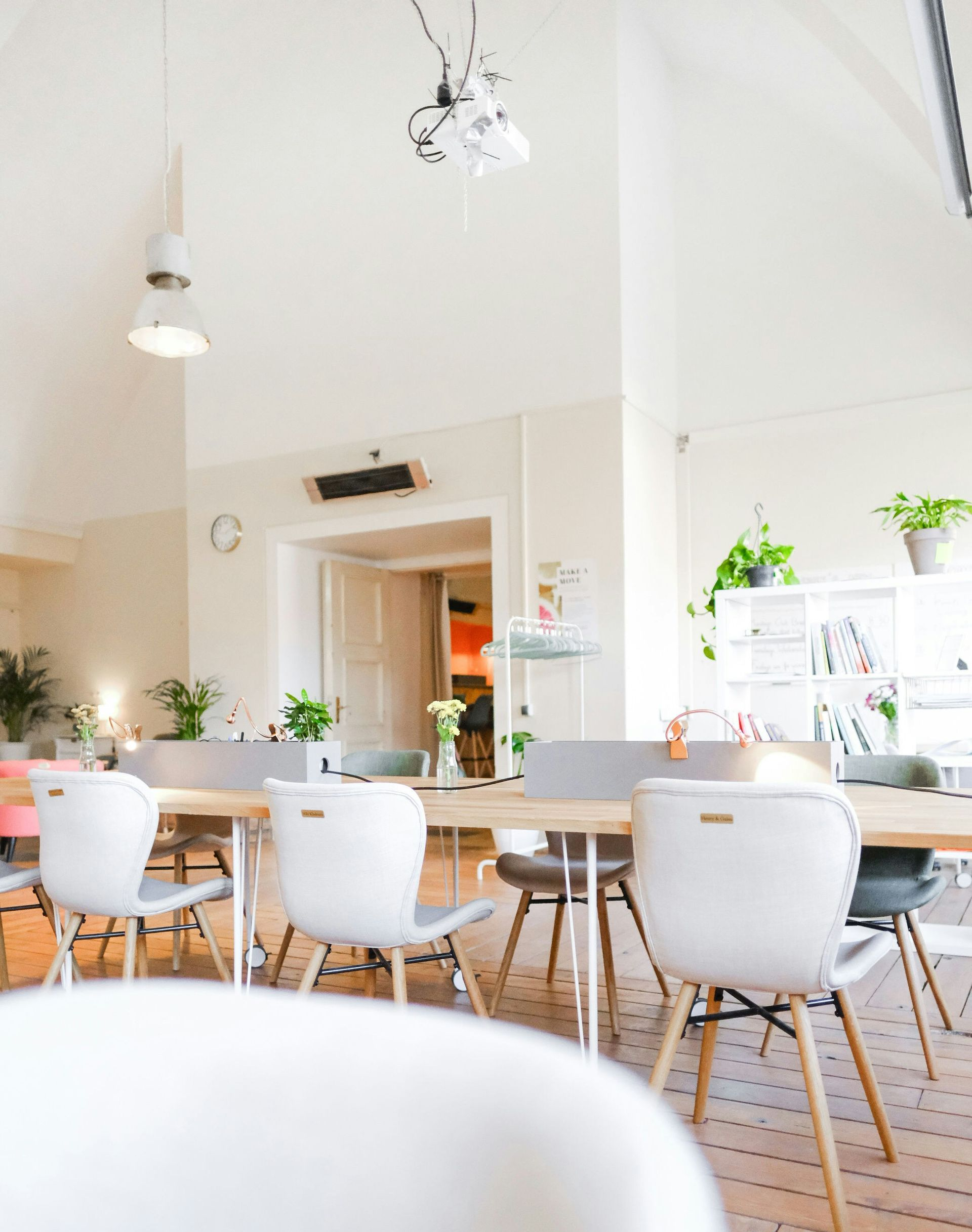 Bright, airy cafe interior with white chairs, wooden tables, hanging lights, and plants on the windowsill