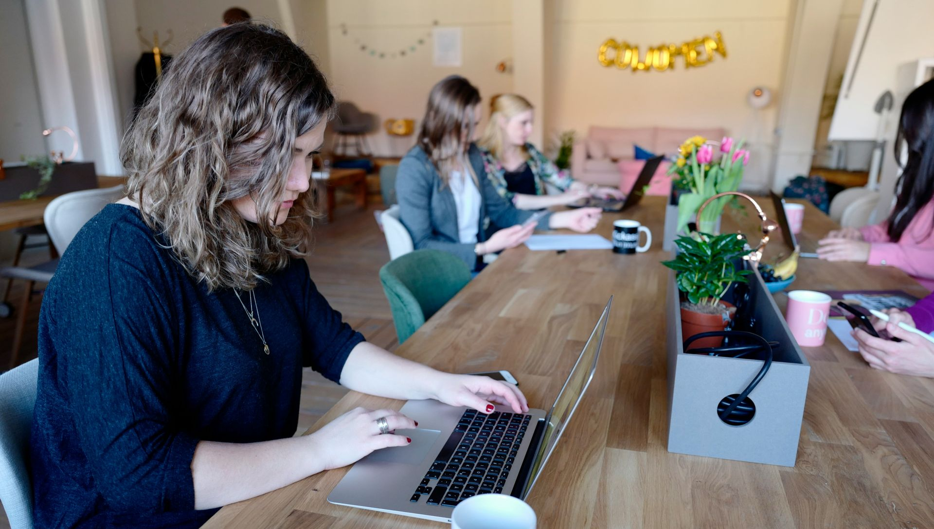 People working on laptops around a wooden table in a bright office meeting space