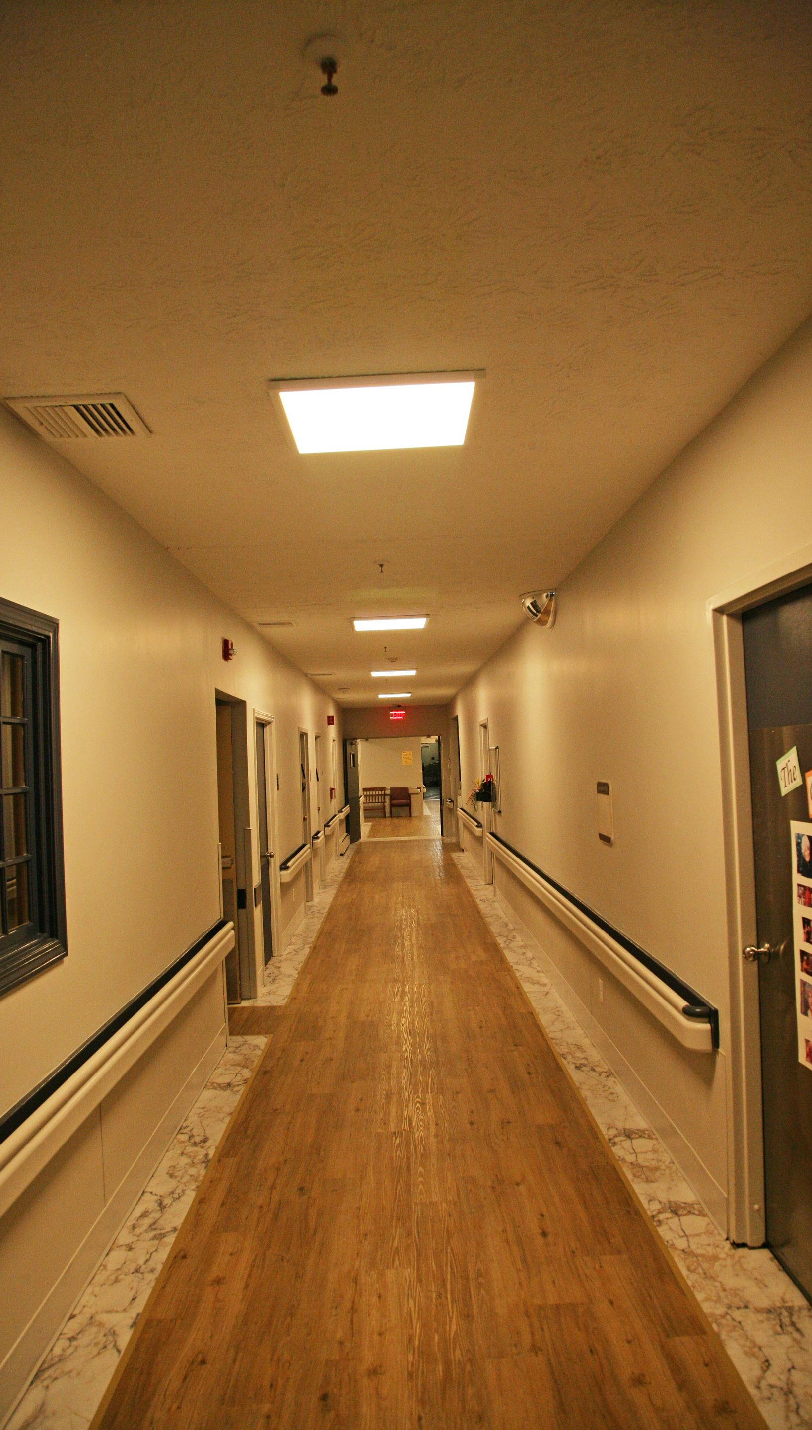 Long, wood-floored hallway with doors and lights. Handrails run along both walls.