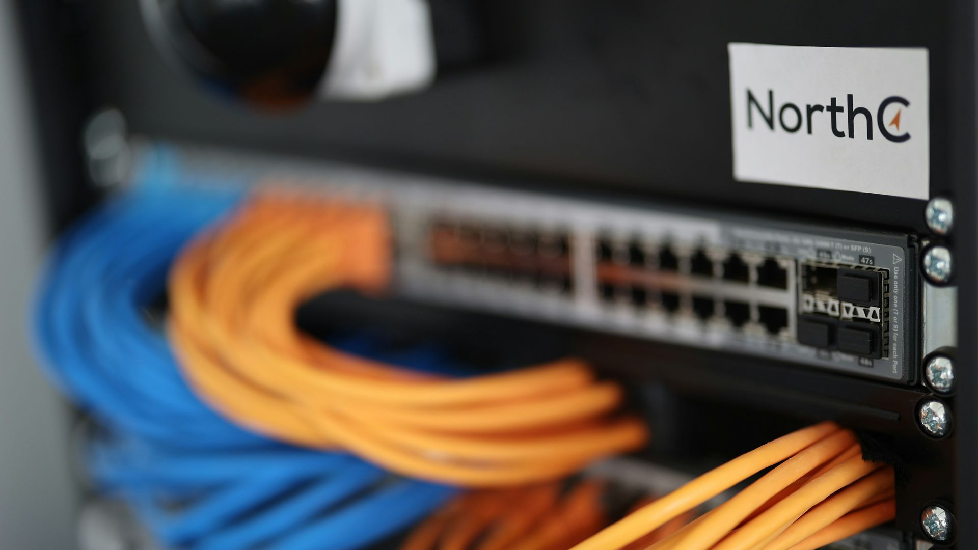 A NorthC data center rack with blue and orange ethernet cables plugged into a networking switch.