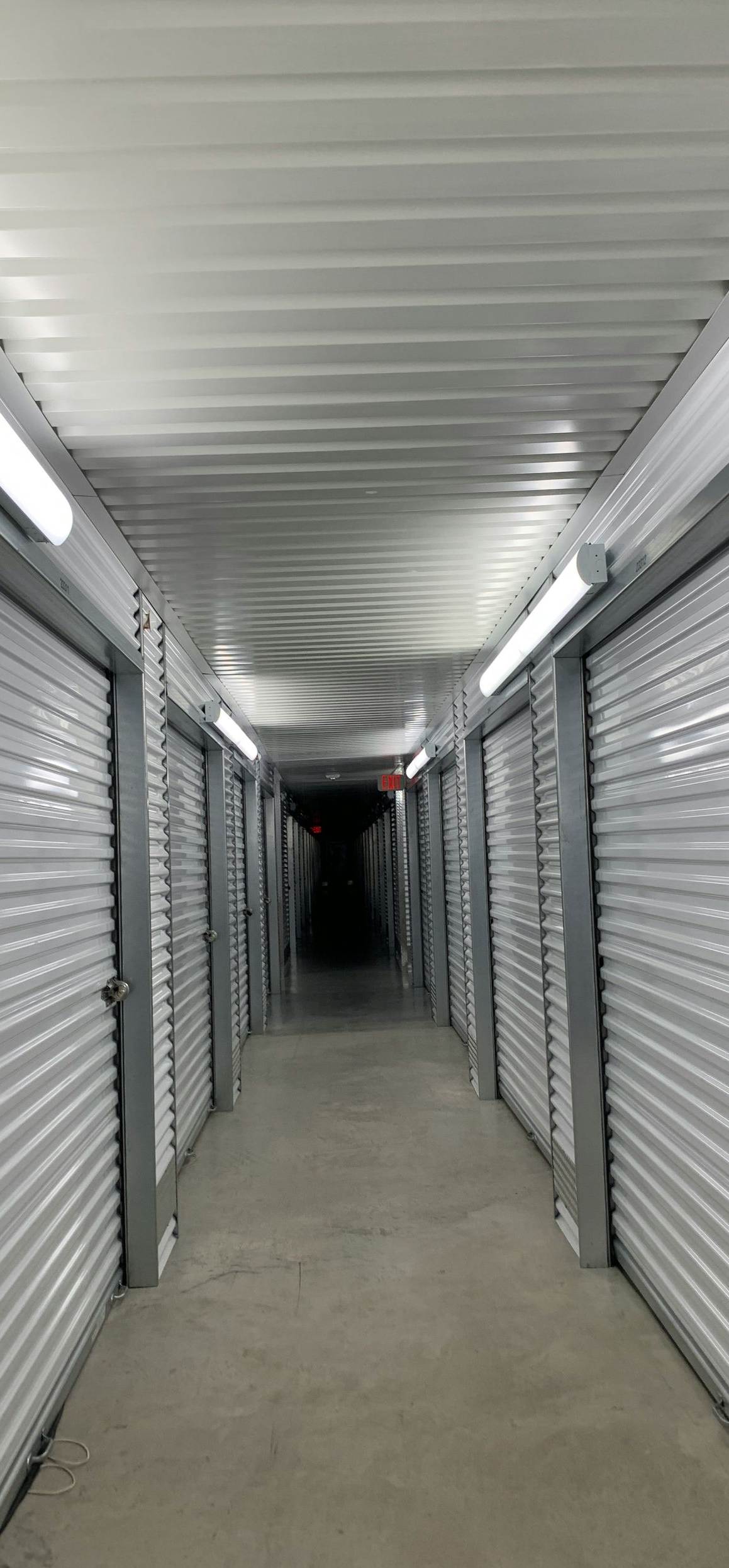 Empty indoor storage unit hallway with white roll-up doors and fluorescent lights