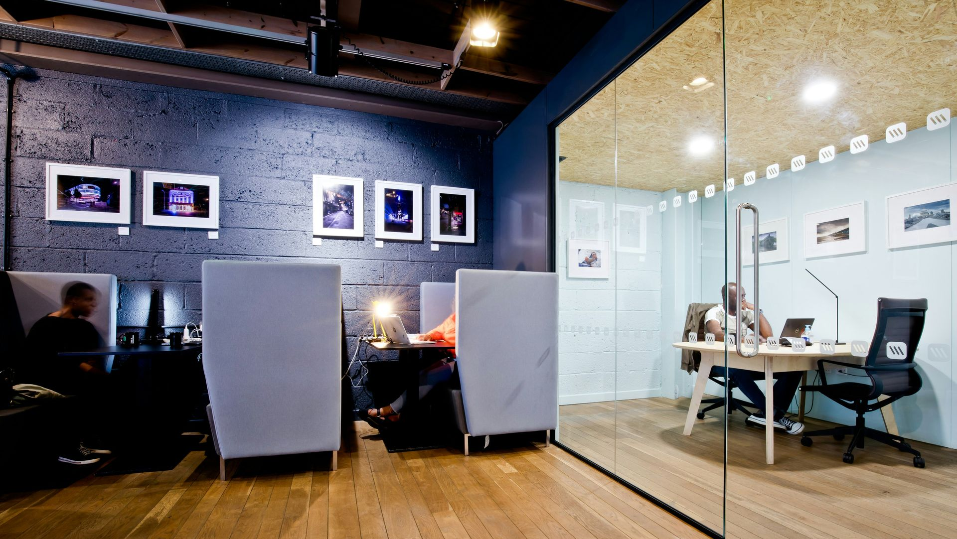 Modern office with glass meeting room, desks, chairs, and framed photos on a dark wall