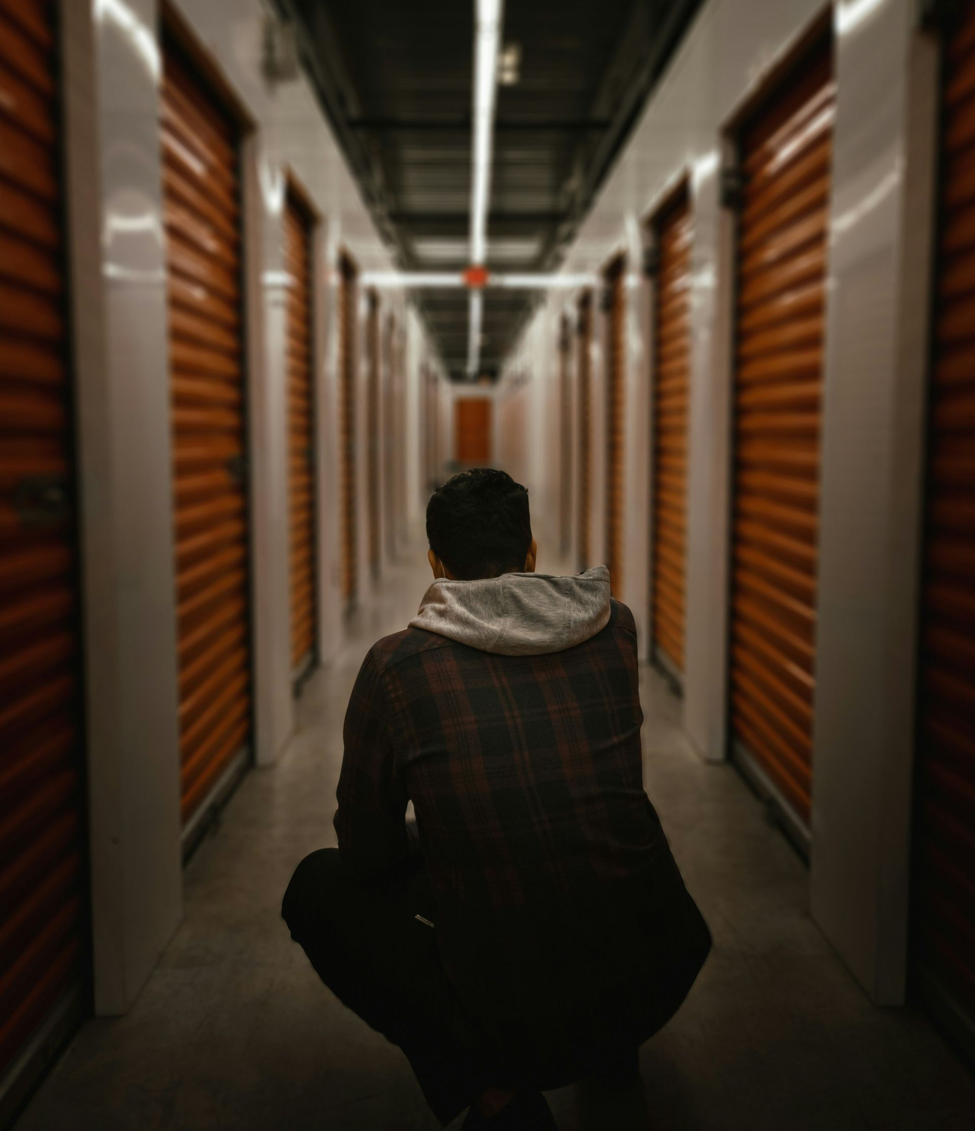 Person crouching in a dim hallway lined with orange storage unit doors