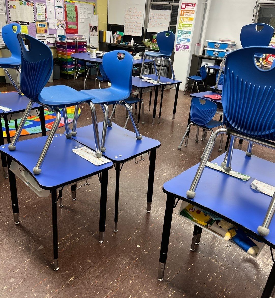 Blue chairs stacked on blue desks in a classroom, prepared for cleaning or rearranging.