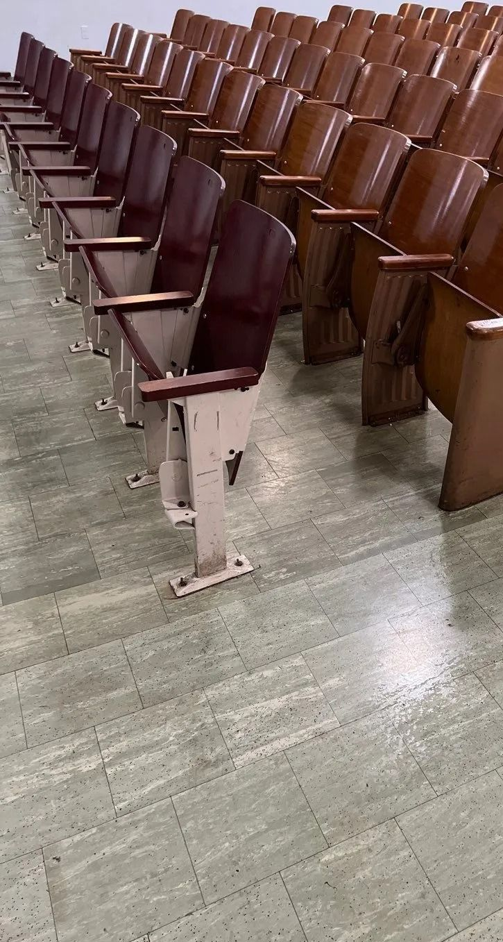Rows of empty, wooden auditorium seats on a gray tiled floor.