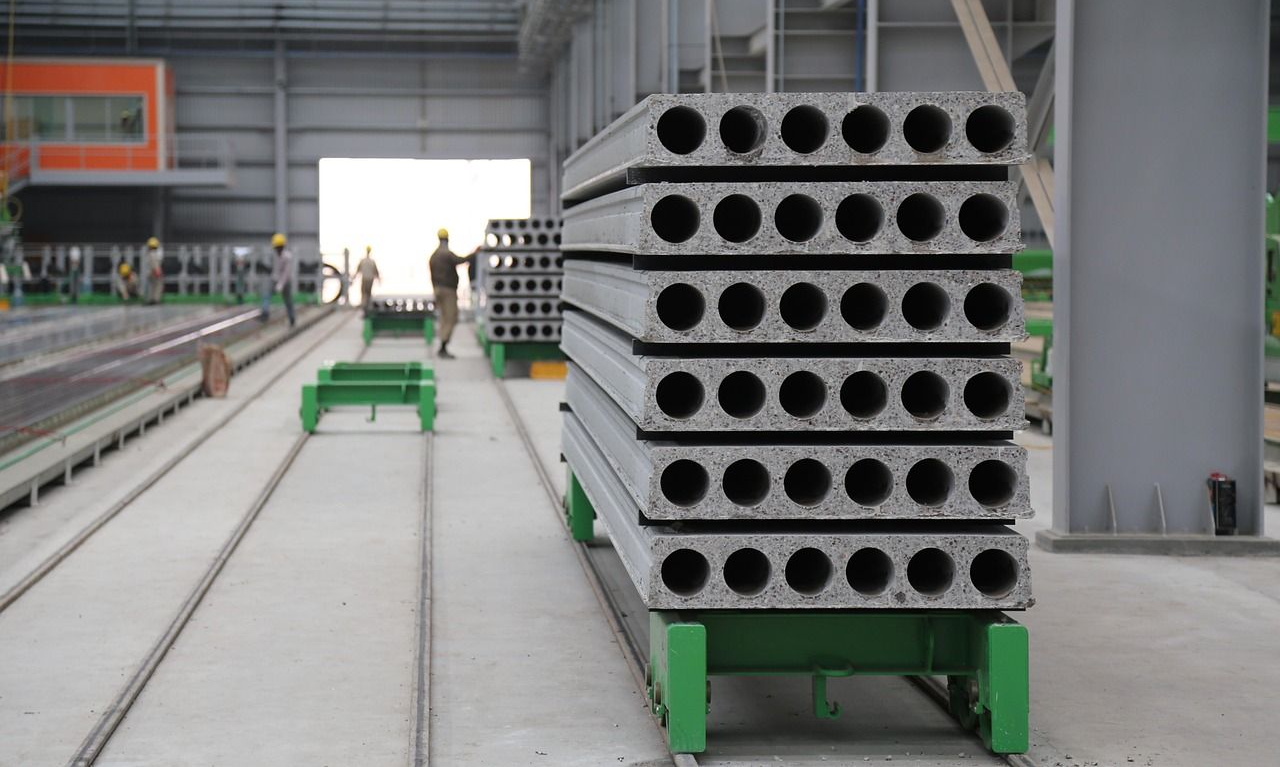Stacked concrete hollow core slabs on a green transport cart inside a factory.