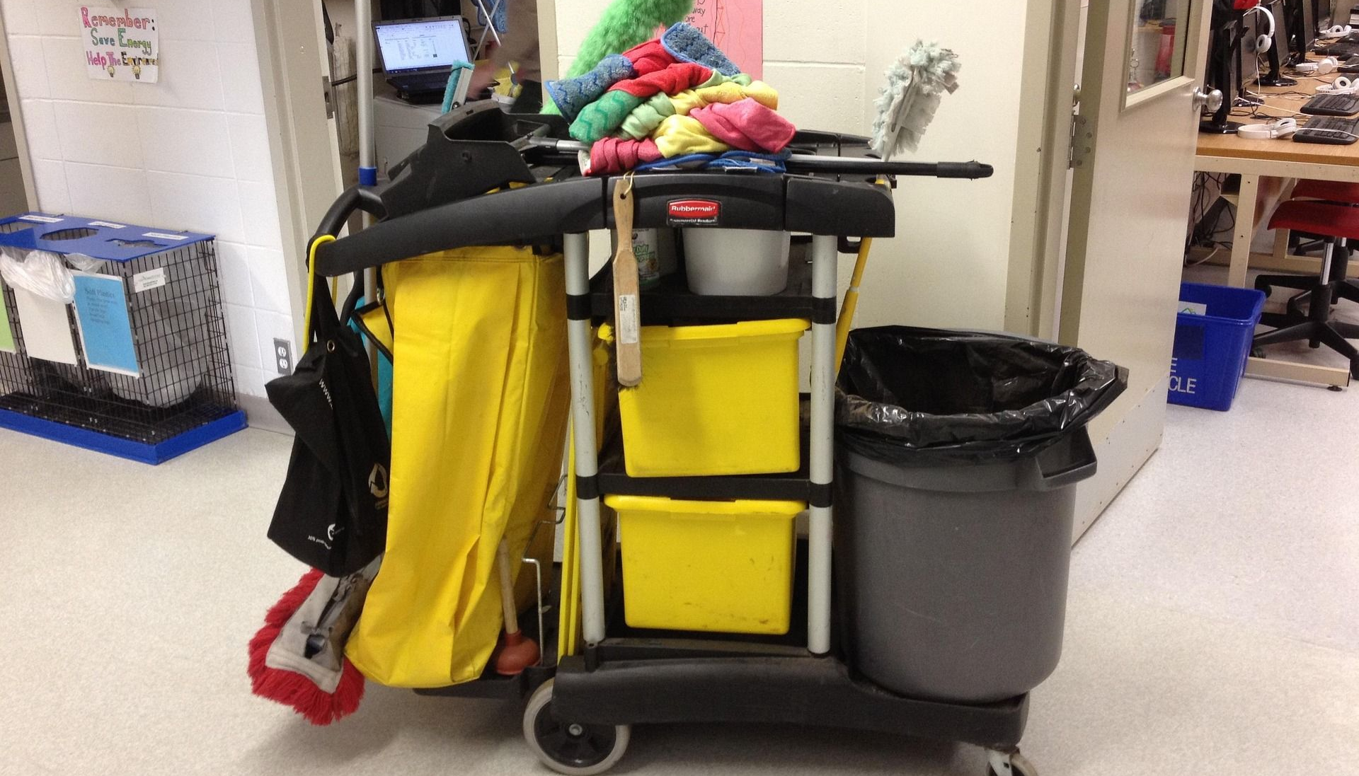Cleaning cart in hallway, with yellow bins, trash can, and cleaning supplies.