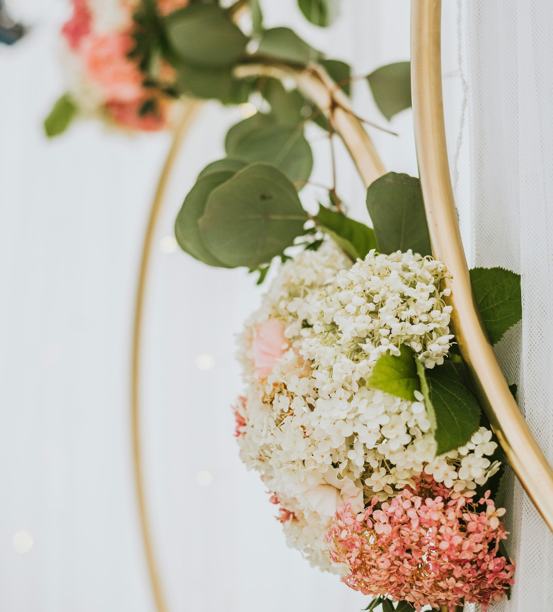 A gold circular frame decorated with green eucalyptus leaves and a cluster of pink and white hydrangea flowers.