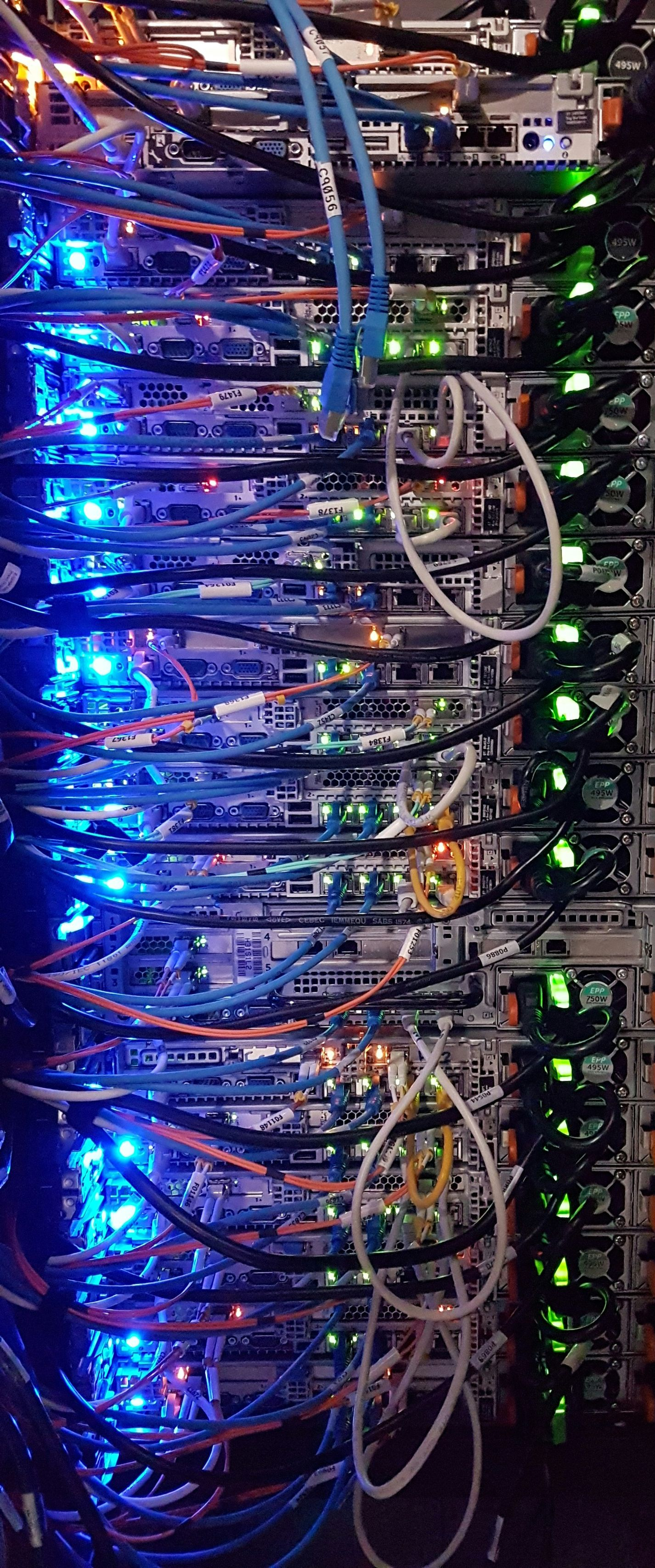 Vertical server rack packed with hardware, dense cabling, and flashing blue and green status lights.