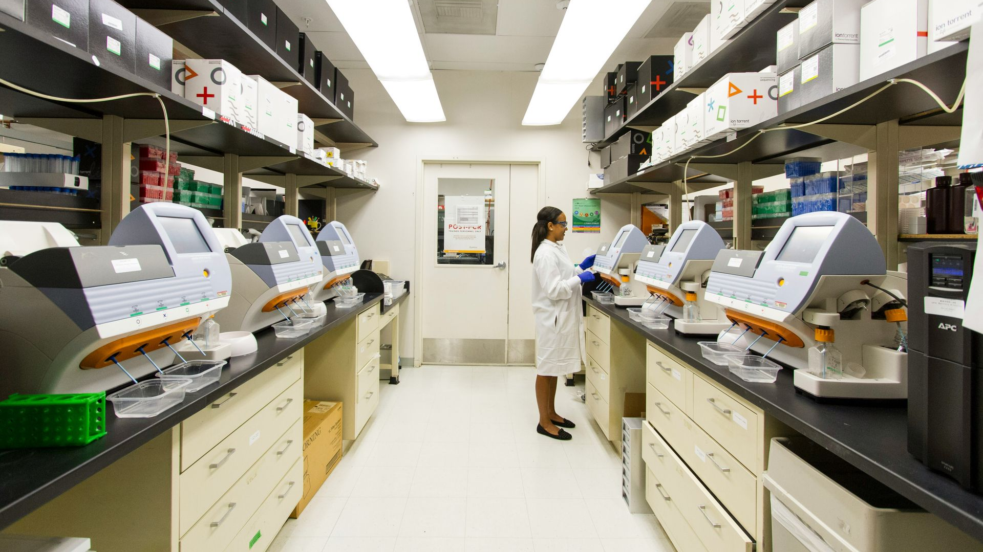 Laboratory with rows of analyzers and a technician in a white coat working at the center.