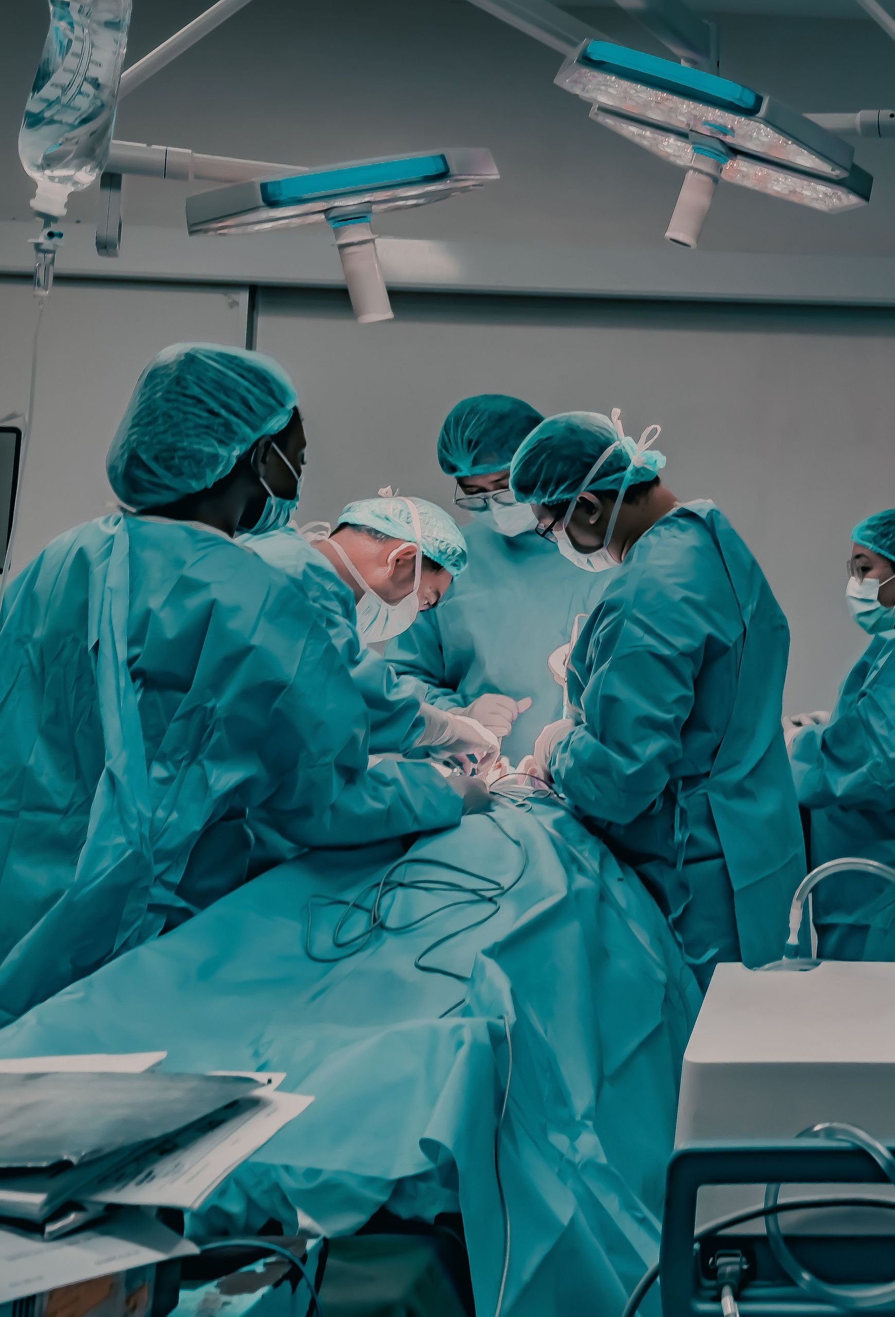 Surgical team in teal scrubs performs an operation under bright operating room lights.