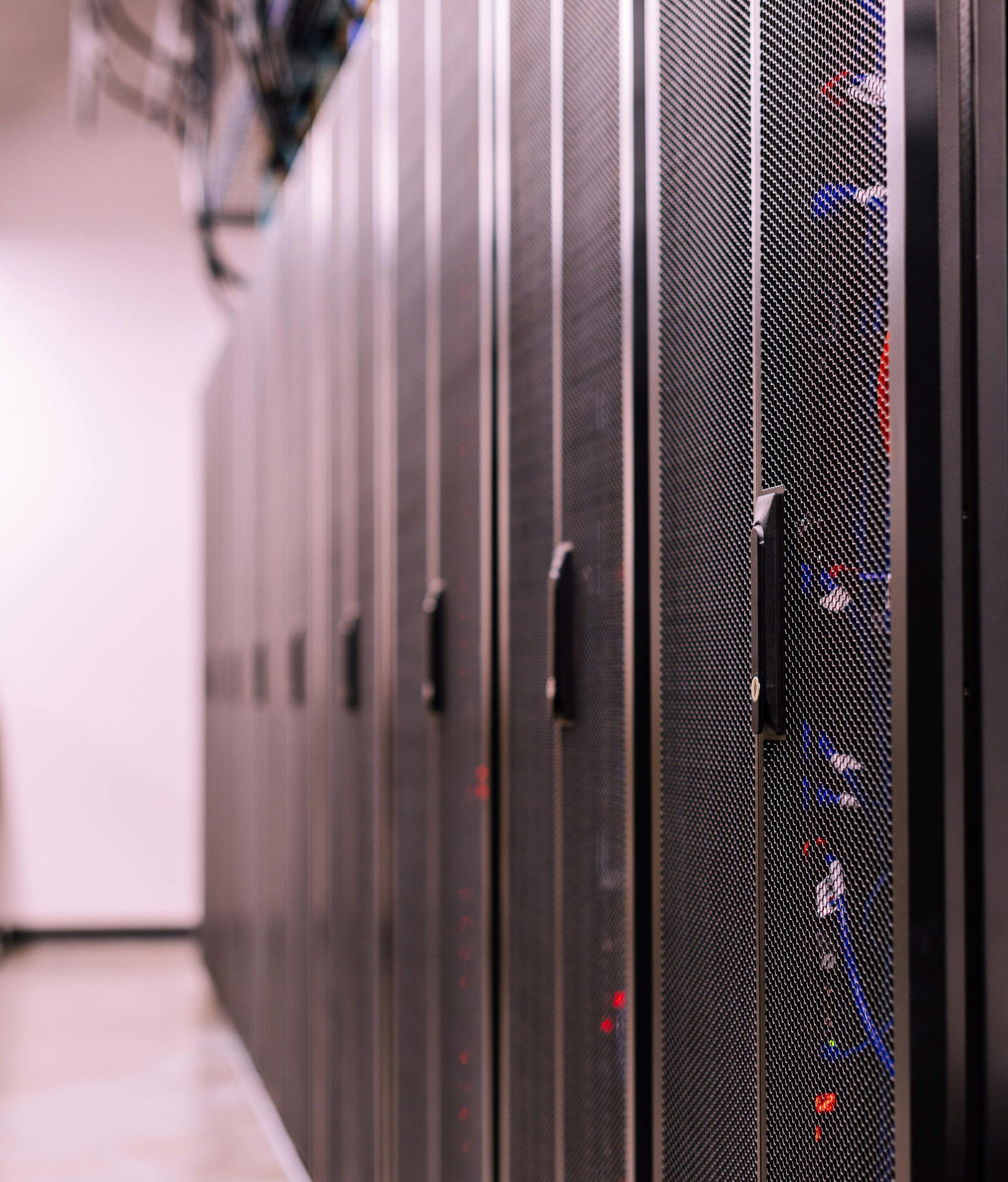 A perspective view of a row of dark metal server racks with mesh doors in a sterile, brightly lit data center.