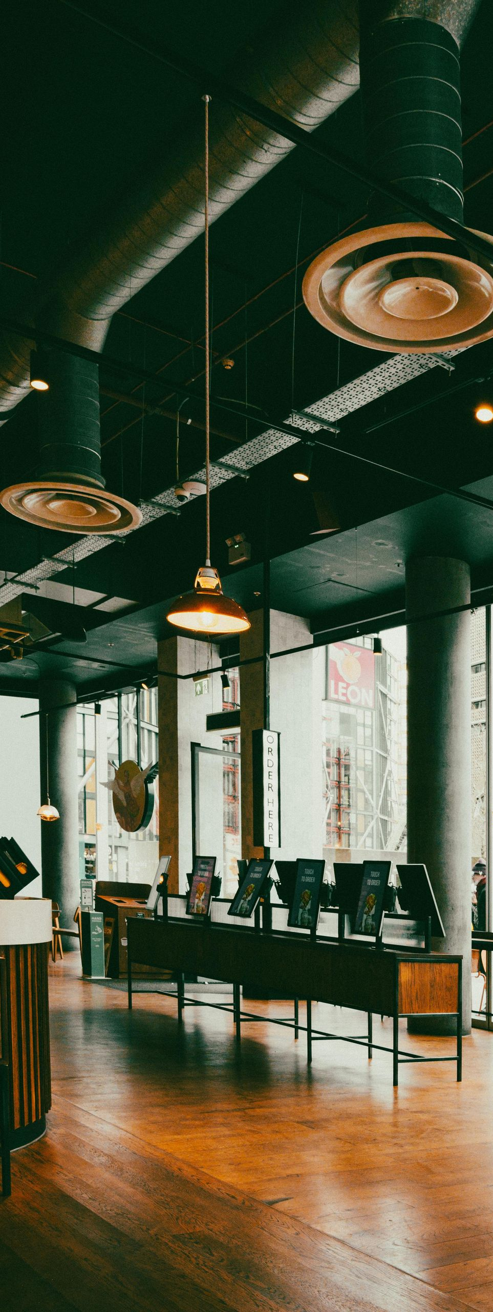 Modern café interior with wooden tables, large windows, hanging lights, and an open industrial ceiling