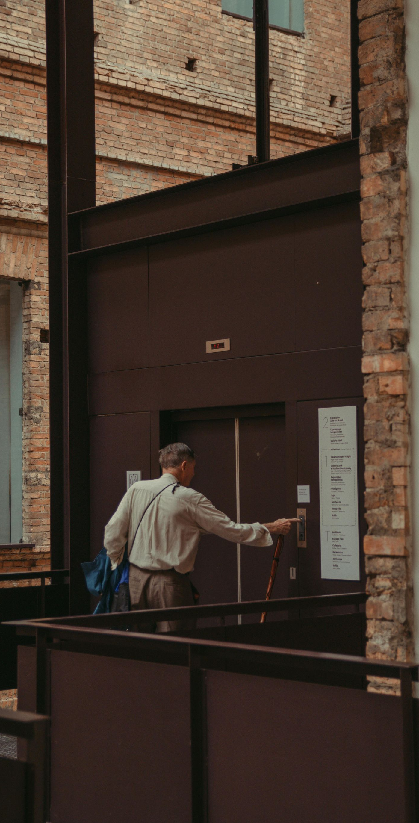 Person in light shirt presses elevator button in a brick building.