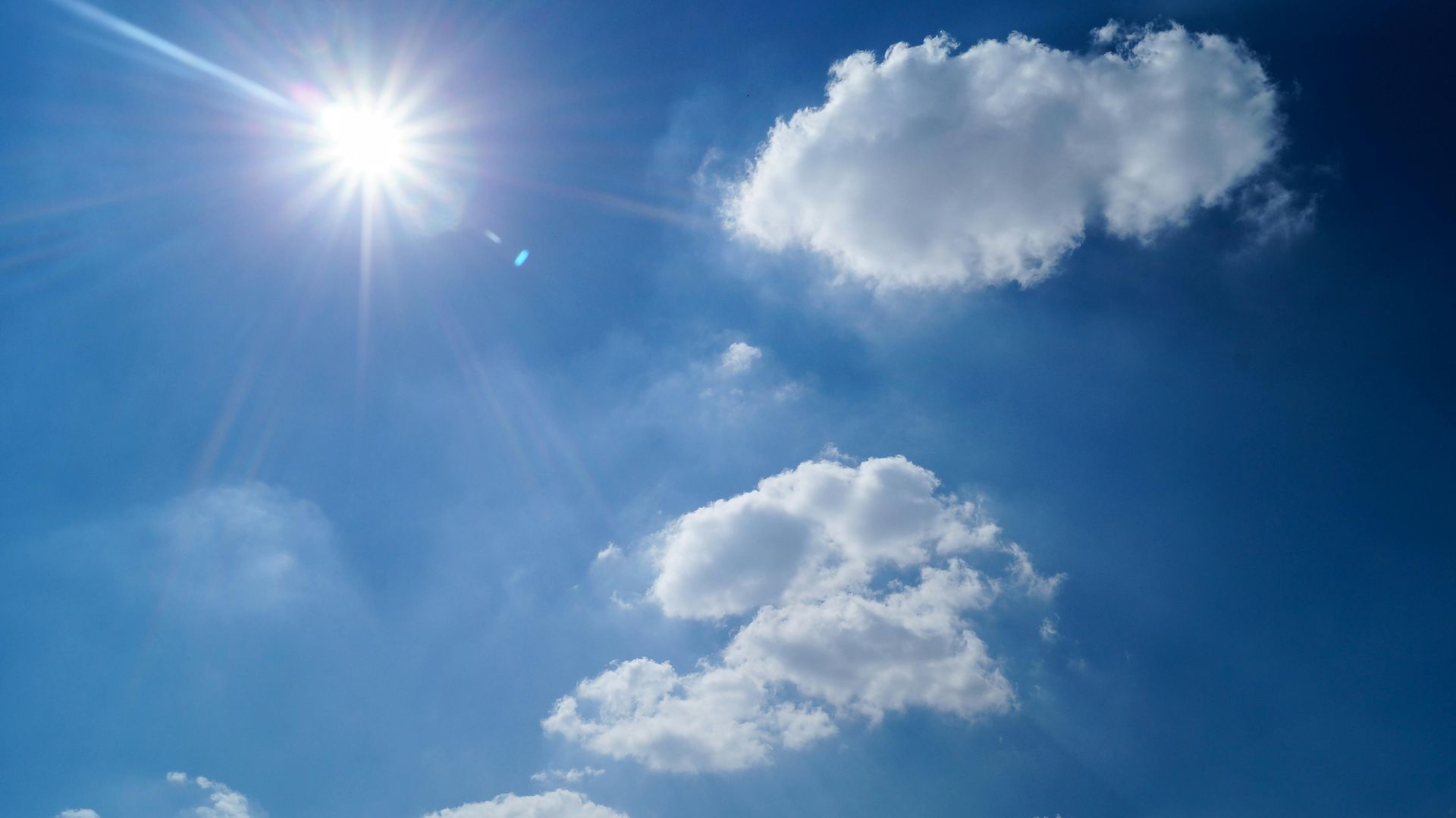 Bright blue sky with the sun shining and a few white clouds