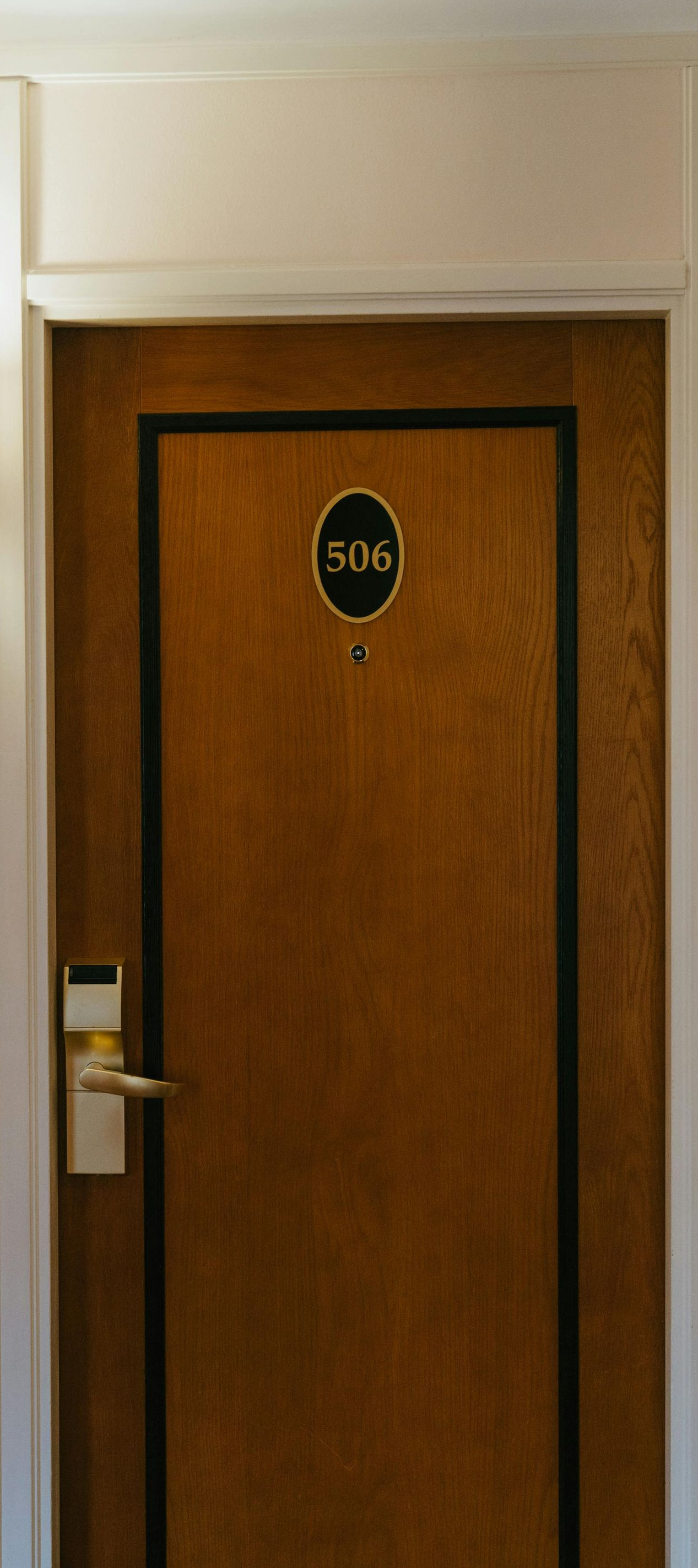 Hotel room door, brown wood with black trim, number 506. Gold wall sconce to the left.