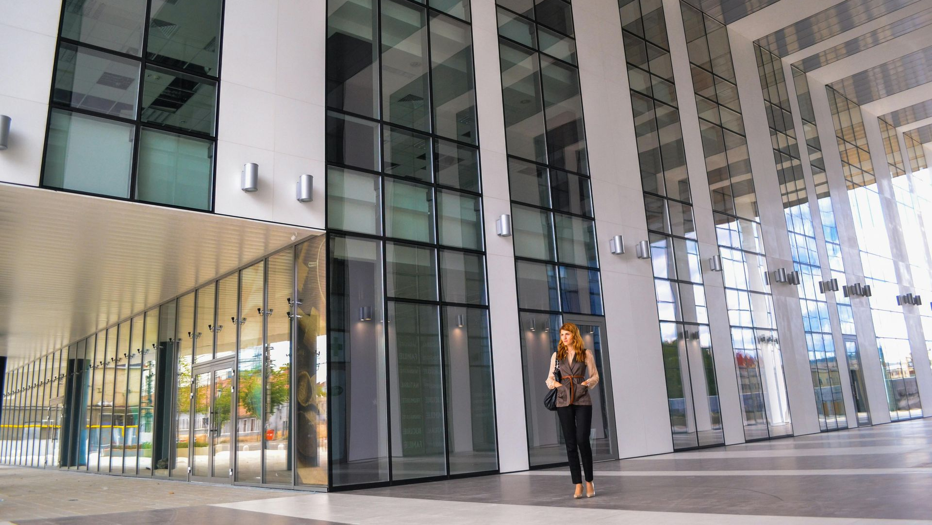 Woman standing in a modern building with large glass windows and white pillars.