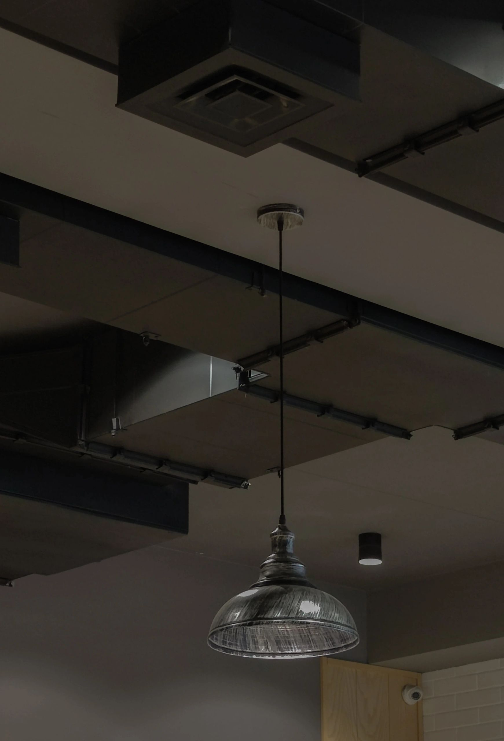 Hanging pendant lamp beneath a dark industrial ceiling with exposed beams and ducts