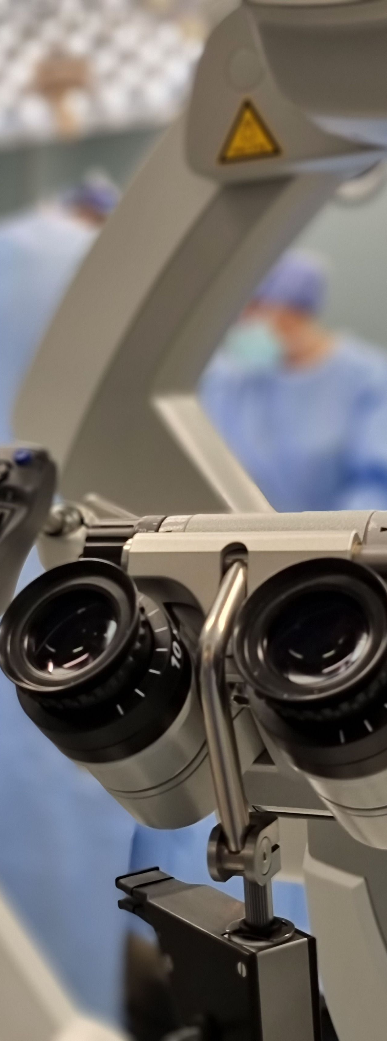 Close-up of a surgical microscope in an operating room, with a blurred medical staff background
