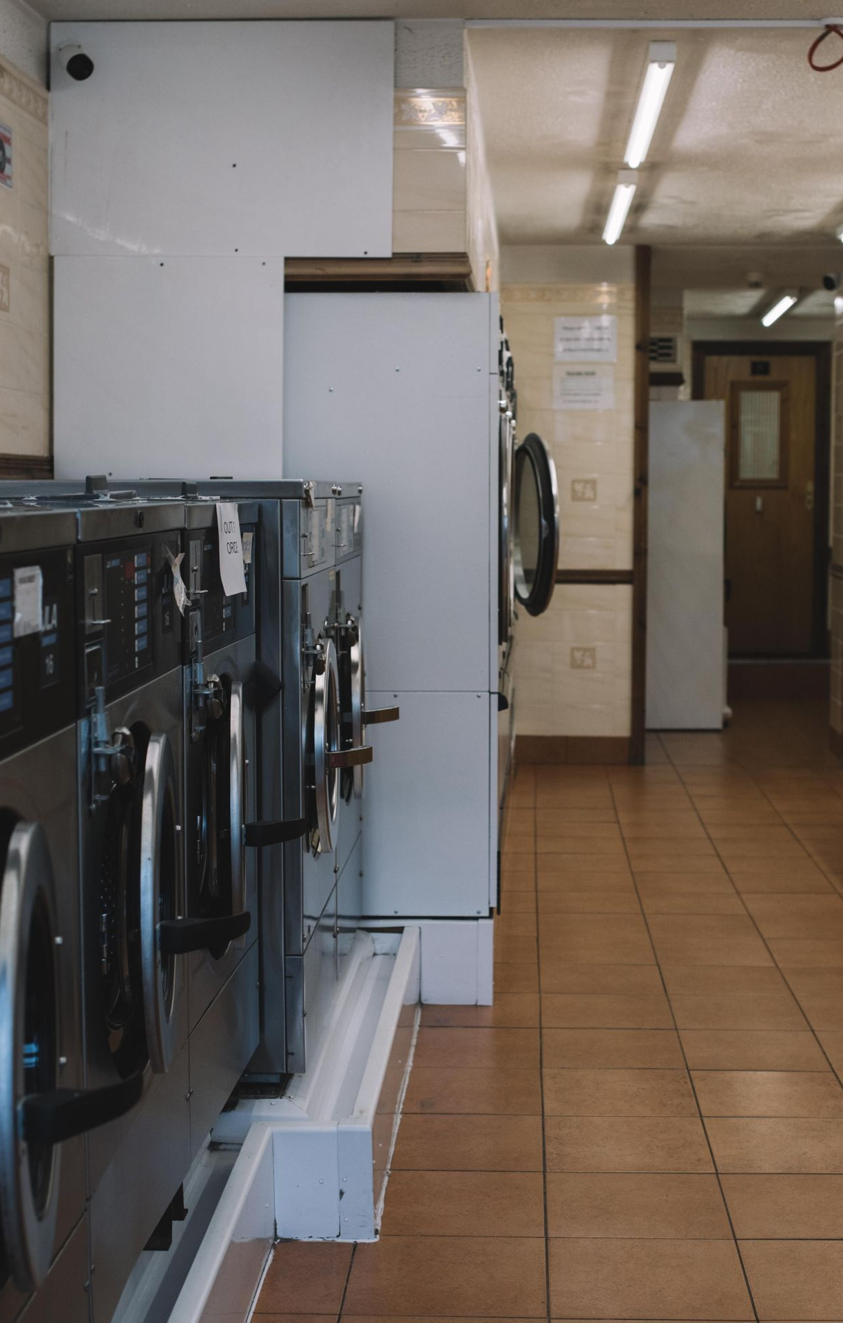Laundry room with rows of washers and dryers, tan tile floor, and counters along the right wall.