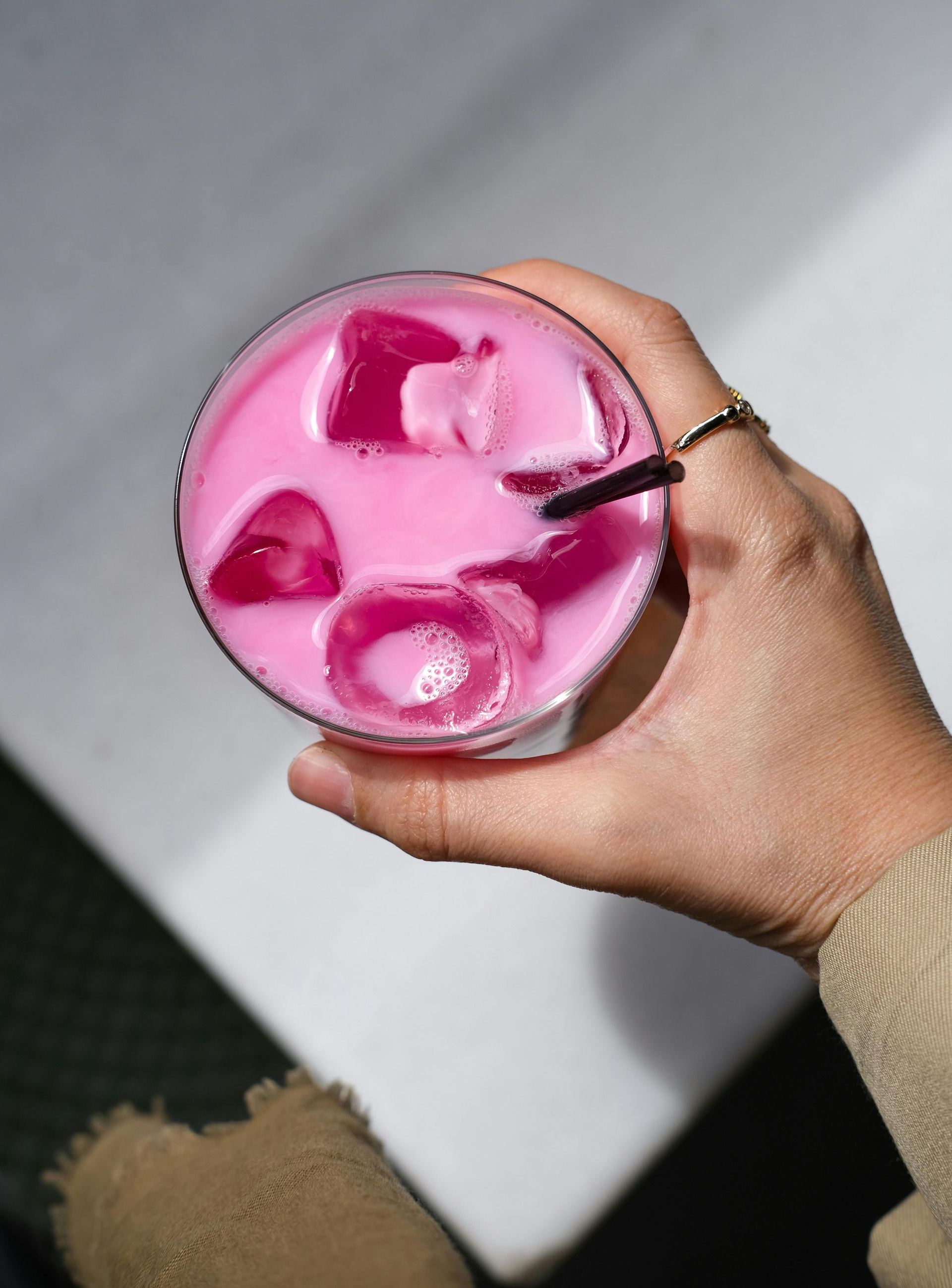 Hand holding a pink iced drink with ice cubes and a black straw