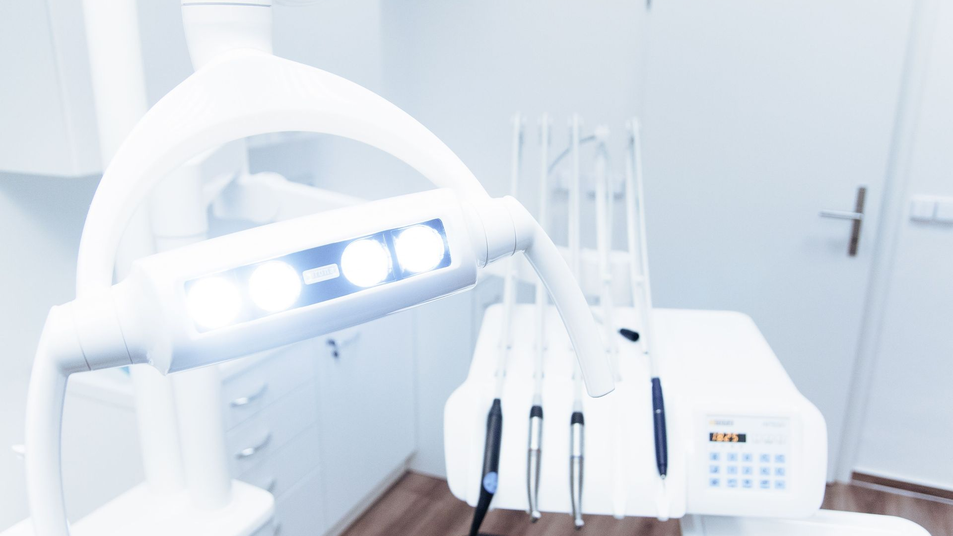 Bright white dental clinic with a reclining chair, overhead lights, and dental tools