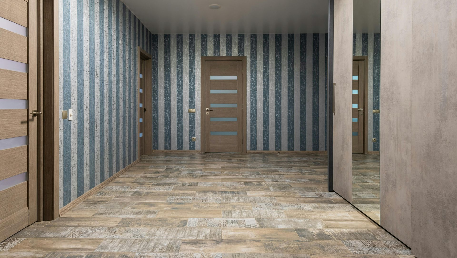 Hallway with blue striped wallpaper, wooden doors, and wood-look flooring.